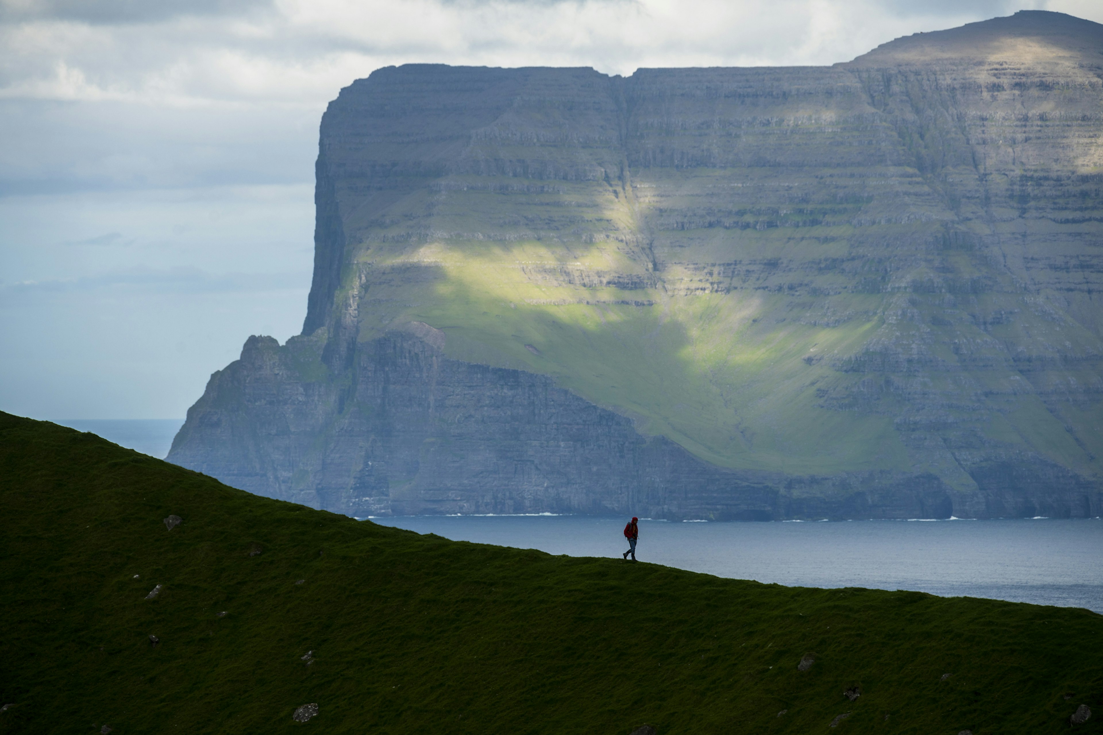 A hiker on a mountain ridge looks towards majestic cliffs