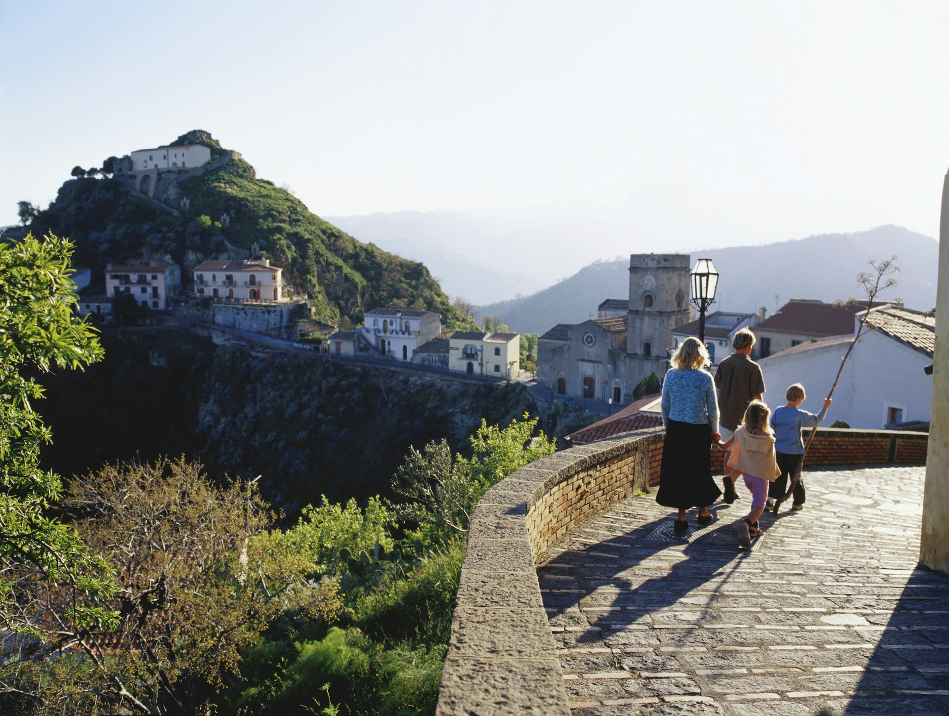 A family of two adults and two small children wander along a path in an inland village, Sicily