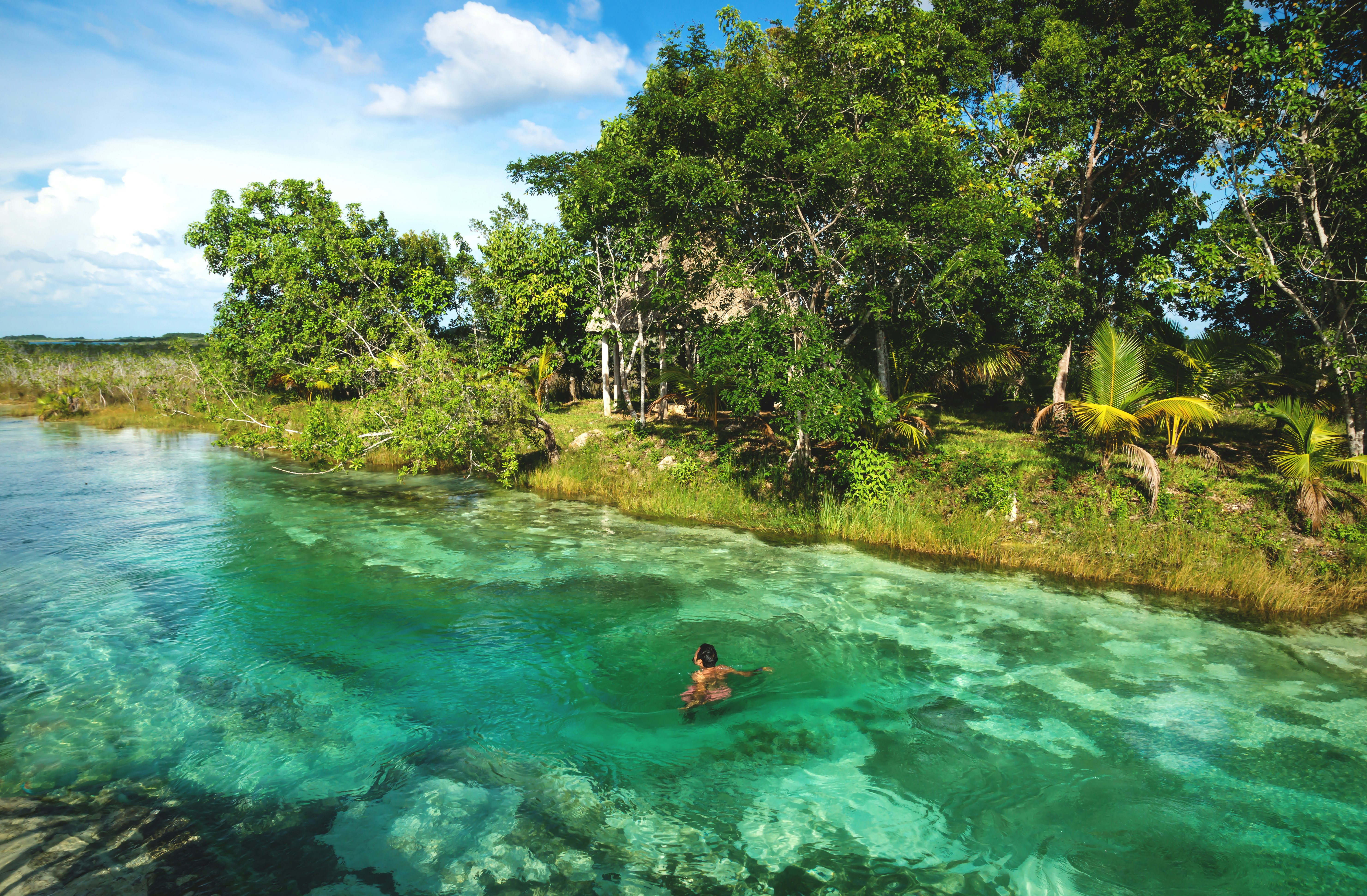 Man in rapids at sunny seven colored lagoon surrounded by tropical plants