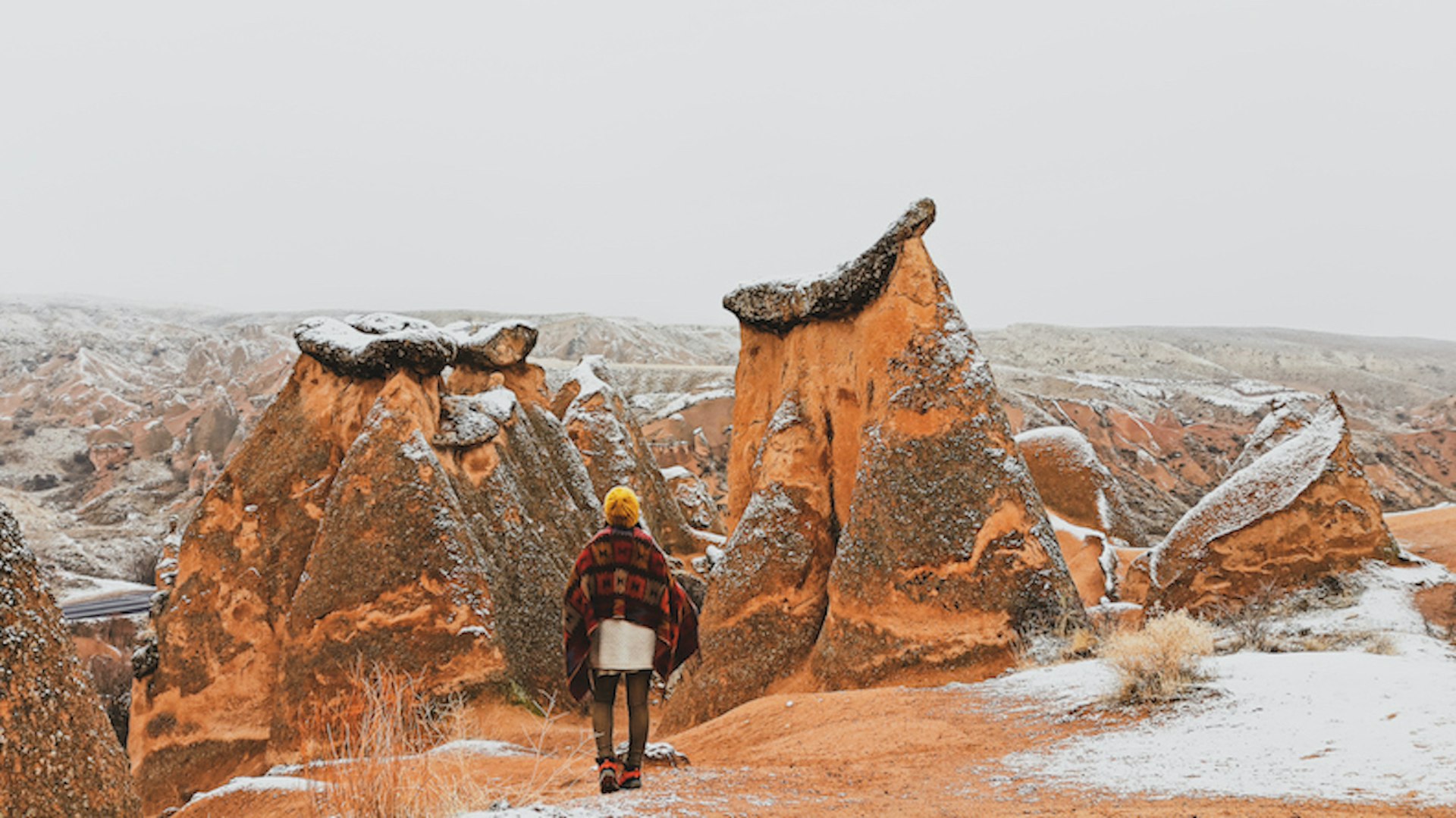 A woman walking around Fairy chimneys surrounded by snow in Imaginary Valley in winter season in Cappadocia.