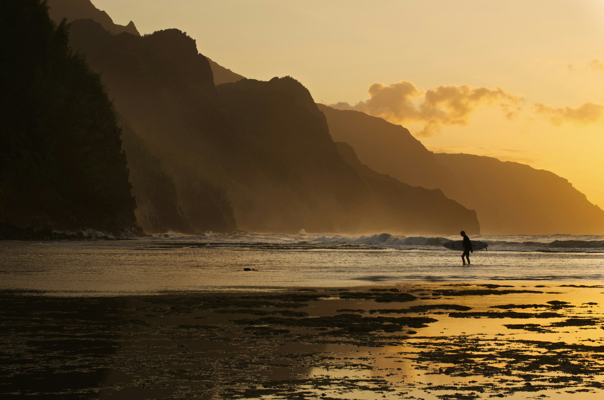 Surfer on the beach and the Na Pali Coast seen from Ke'e beach, Ha'ena, Kauai, Hawaii