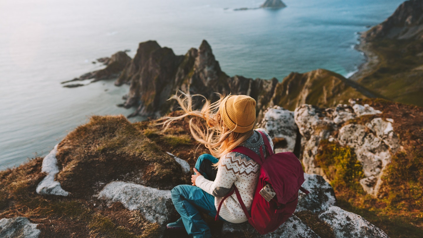 A woman sitting on a rocky outcrop looking down at the sea in Vesteralen, Norway
