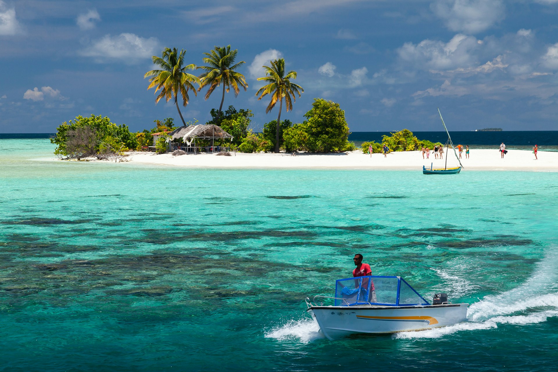 A small speedboat departs from a tiny island where people are gathered