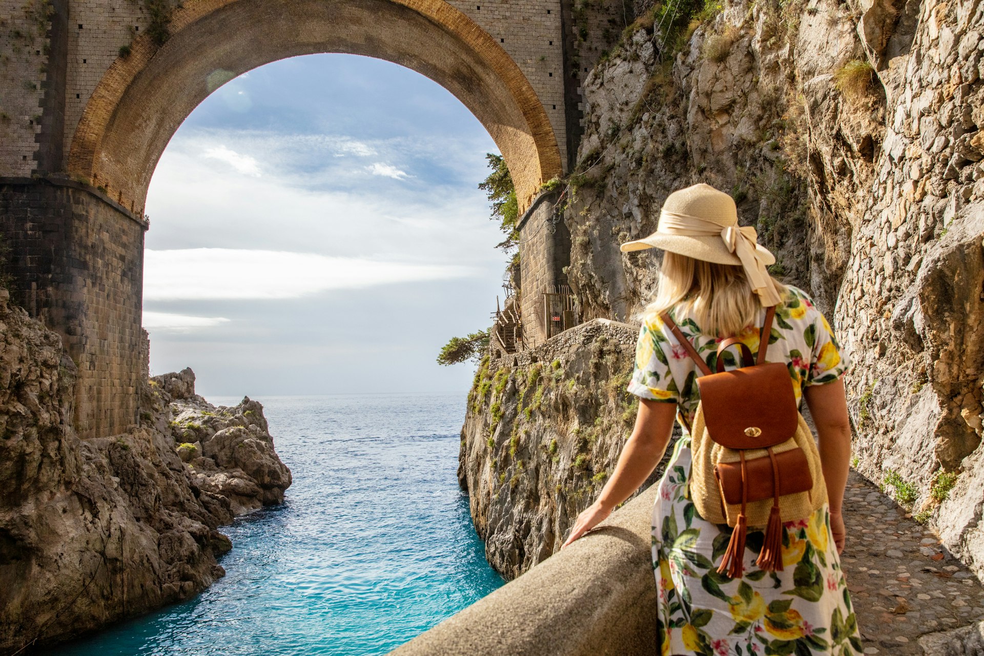 A woman walking along a path beneath the Fiordo di Furore bridge on the Amalfi Coast