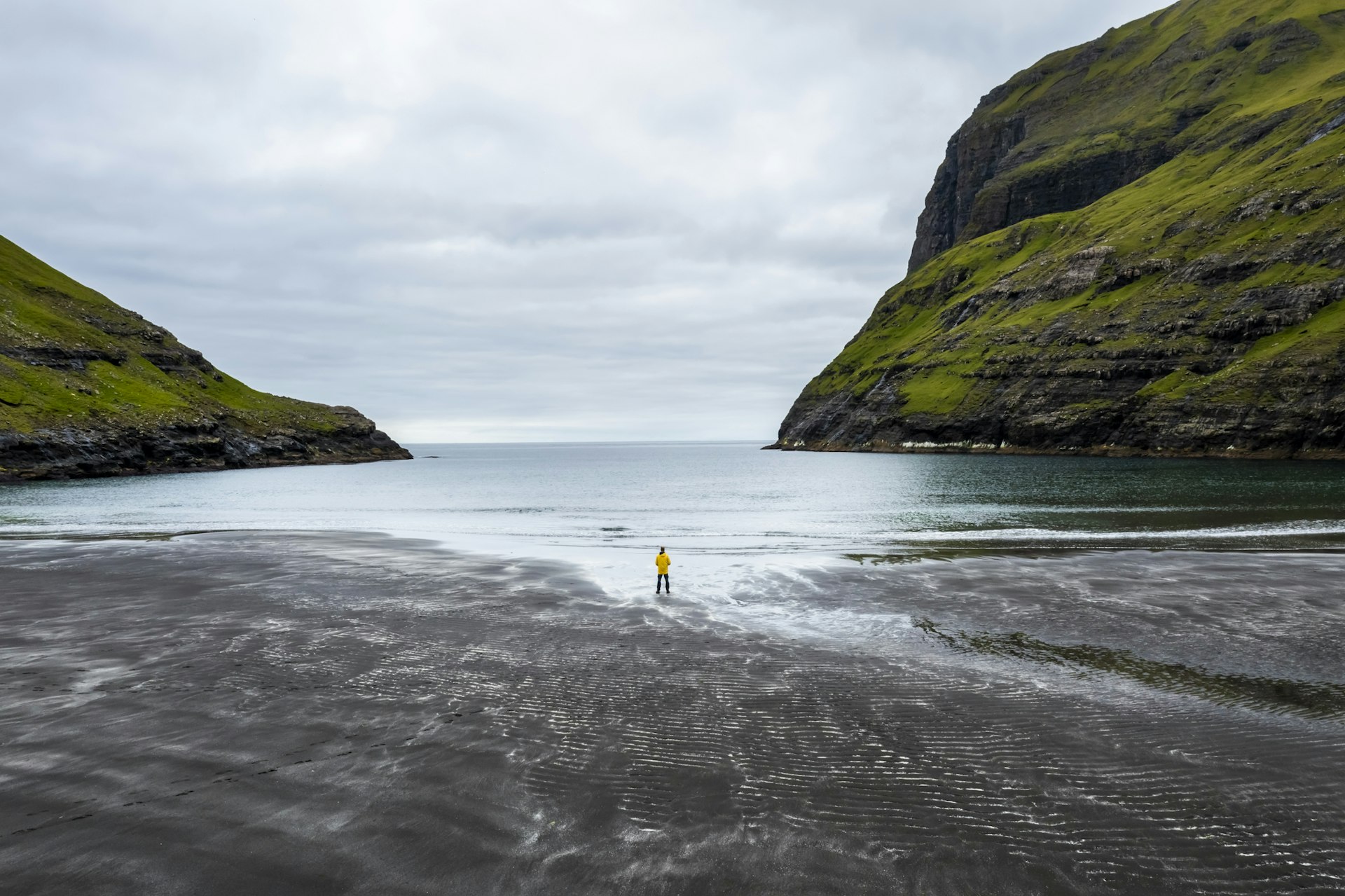 A solo figure stands on a wide windswept beach as rainy weather closes in