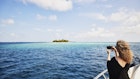 1392627660
Wide shot of mature woman taking photo with smart phone of deserted island from yacht in Indian Ocean in the Maldives