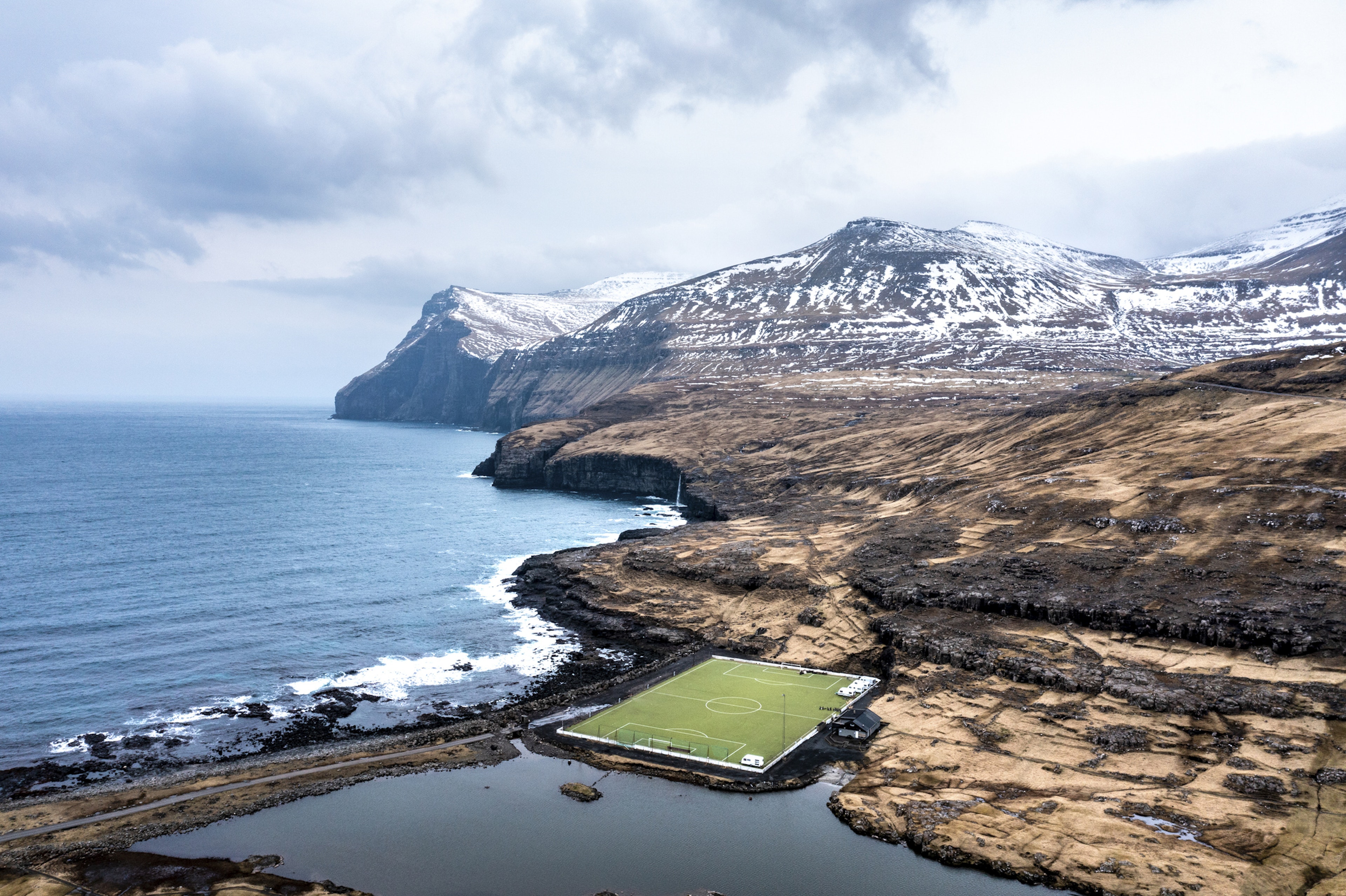 A football field at the very edge of the ocean, with snowy peaks rising behind it