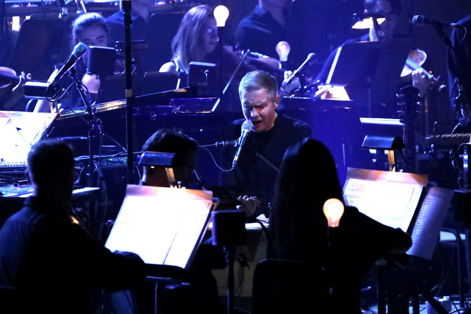 A man sings surrounded by an orchestra of fellow musicians