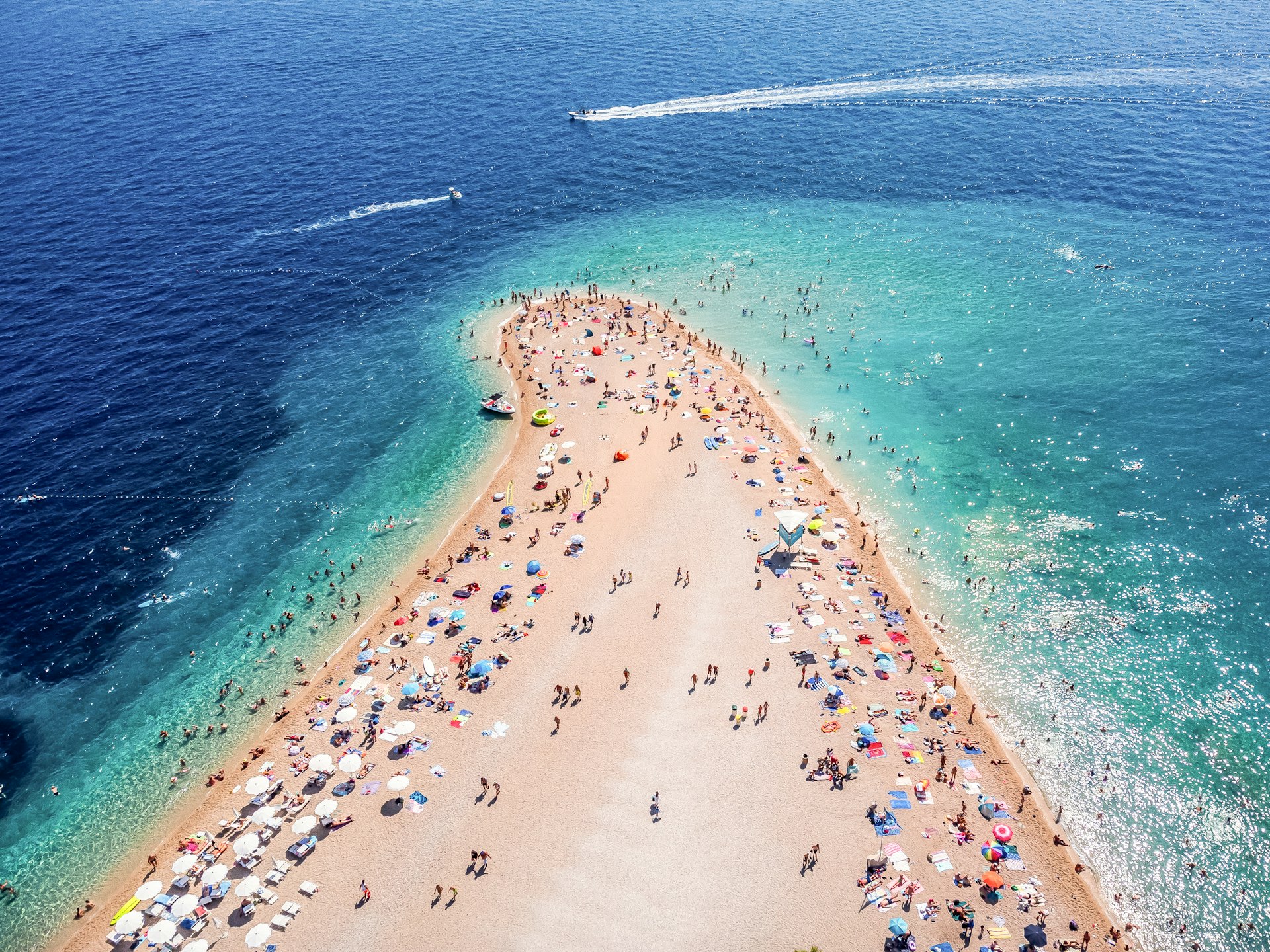 Aerial shot of a beach peninsula, lined with sunshades and umbrellas
