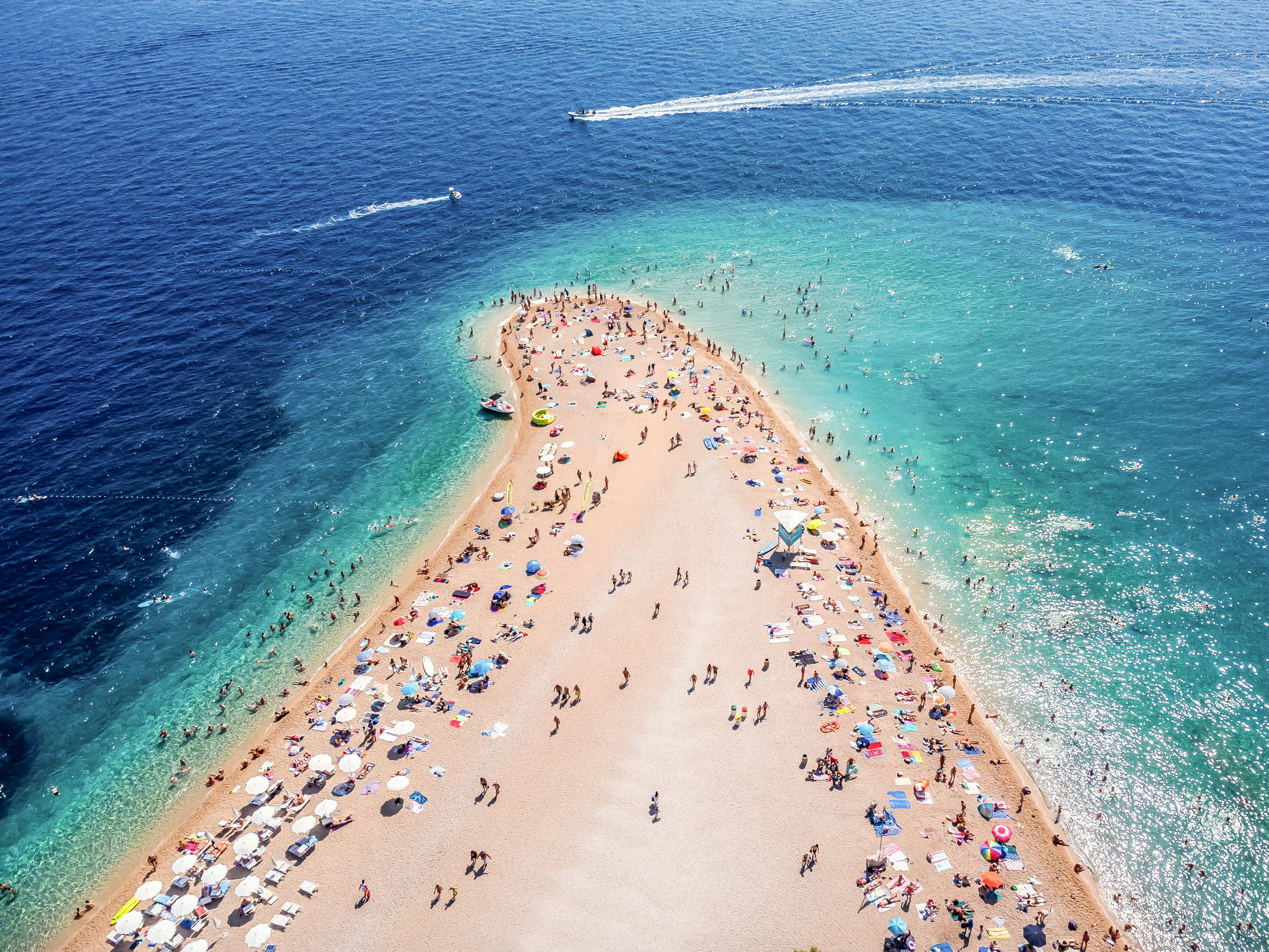 Aerial shot of a beach peninsula, lined with sunshades and umbrellas