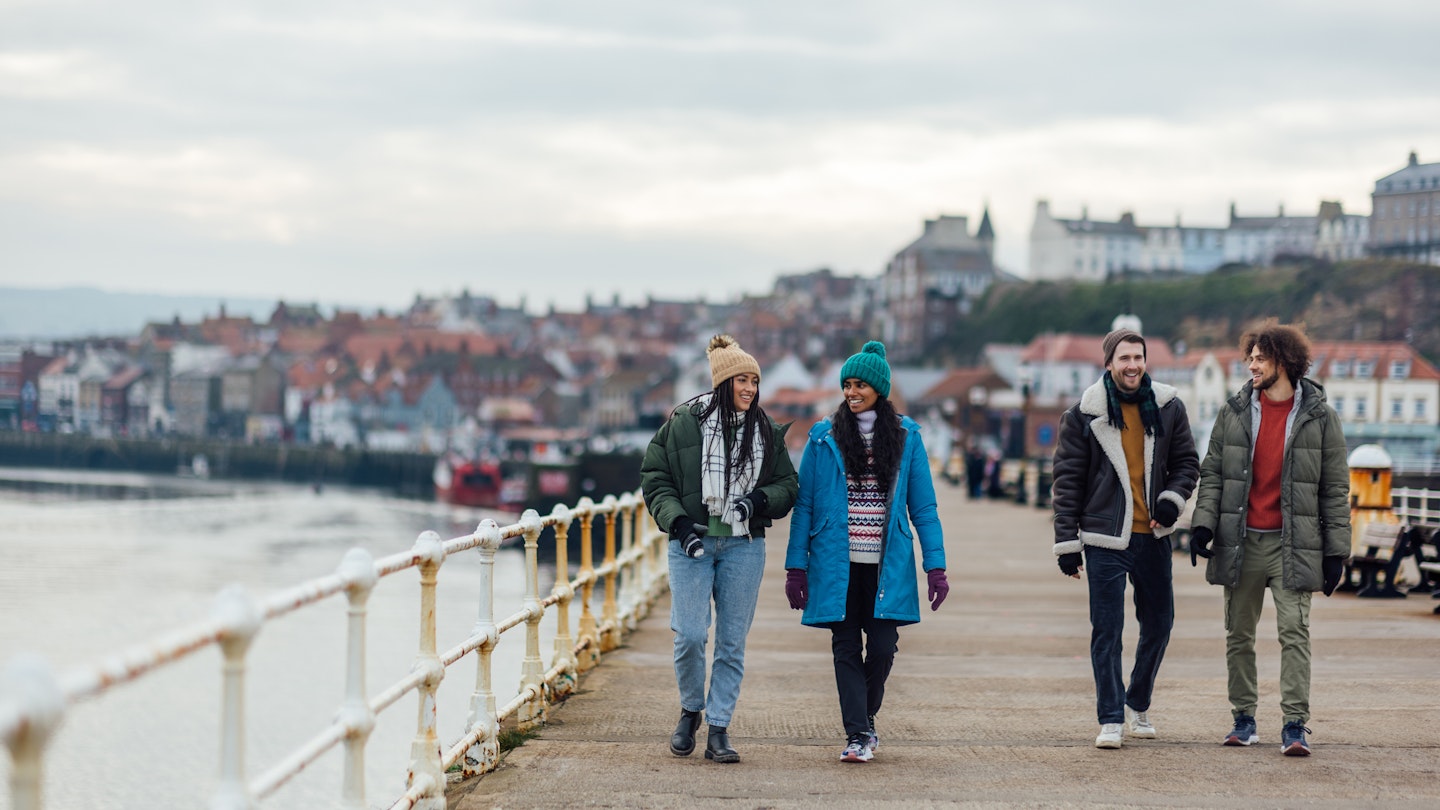 A wide shot of two heterosexual couples wearing warm casual clothing and accessories. They are enjoying a day out in the seaside town of Whitby in February. They are walking along the pier, talking and laughing...Video is also available for this scenario.
1712939087