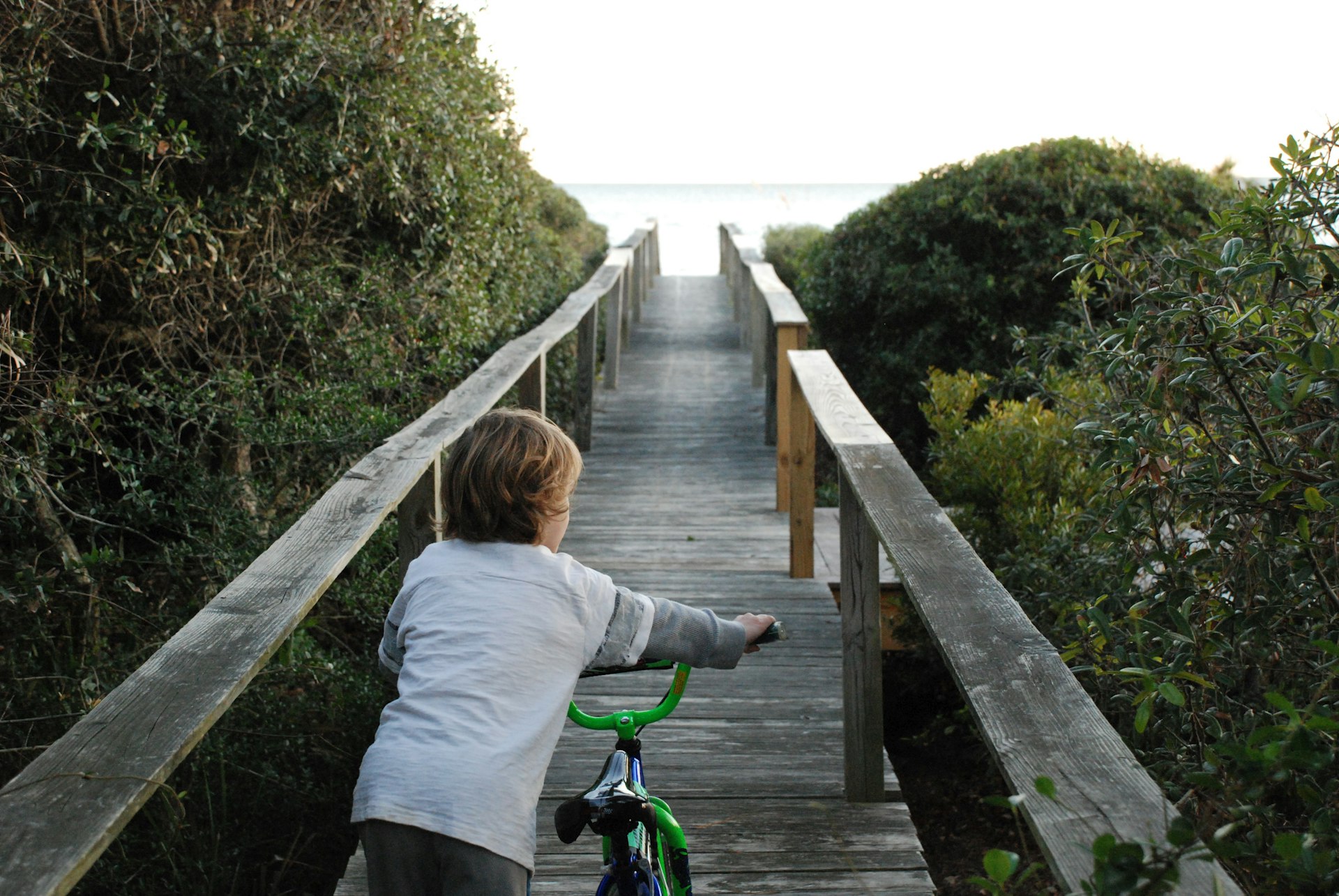 Young boy pushing his bike down a long wooden boardwalk with the ocean in the background, Hilton Head, South Carolina, USA