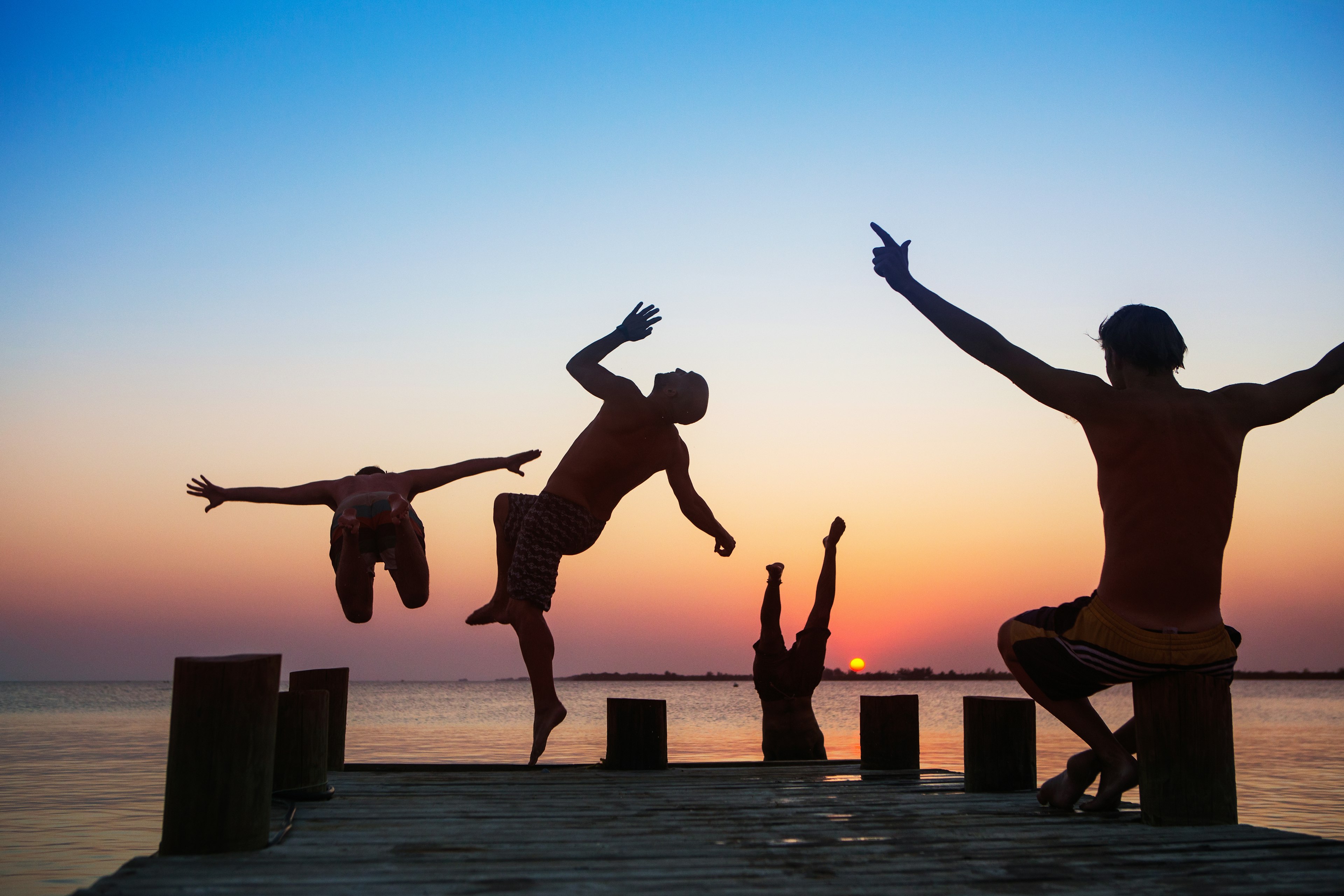 A group of men jump off the end of a pier at sunset