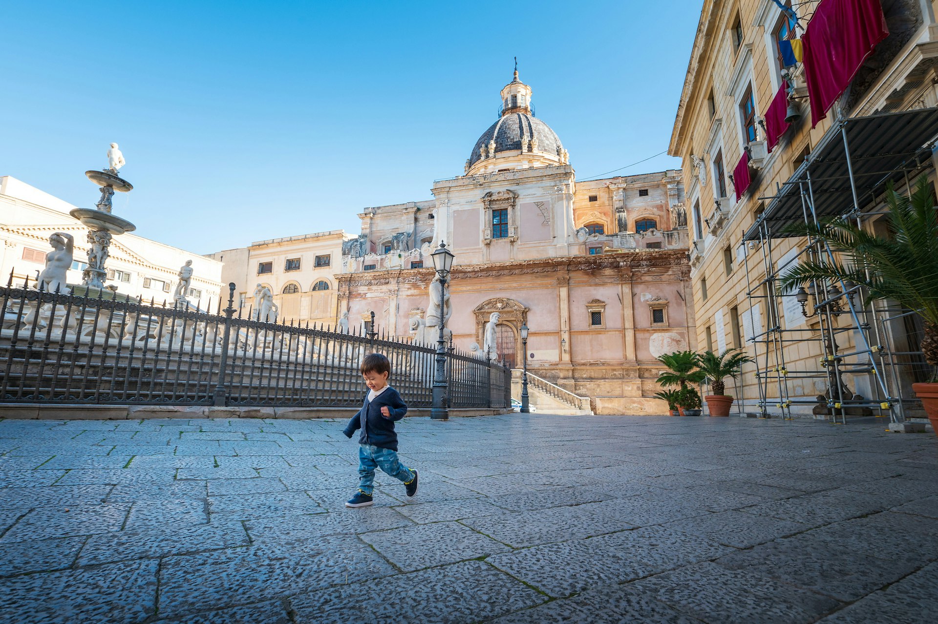 A small toddler wanders around in a public square on a sunny day