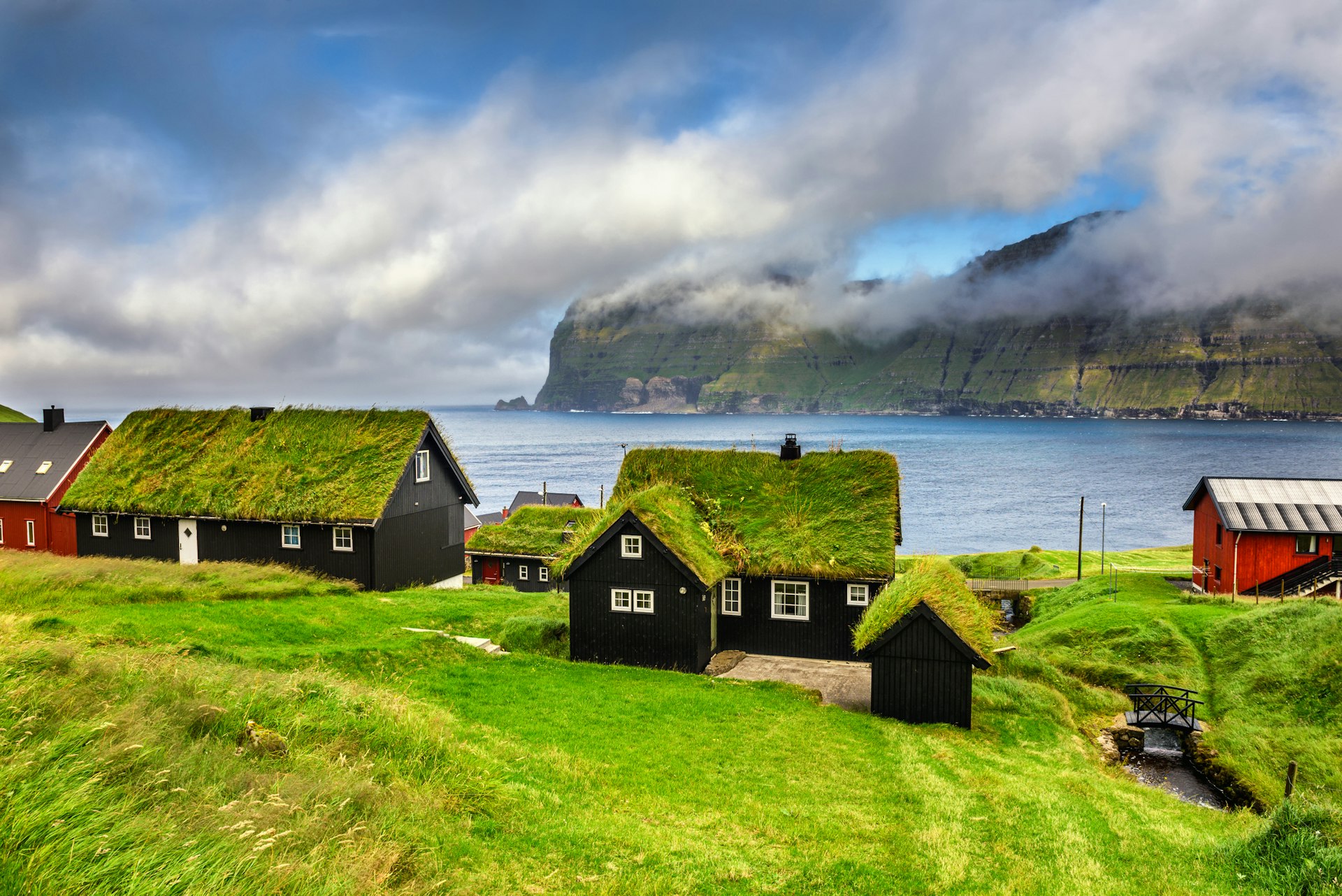 Grass-covered houses sit on the lush coast of the Faroe Islands. 