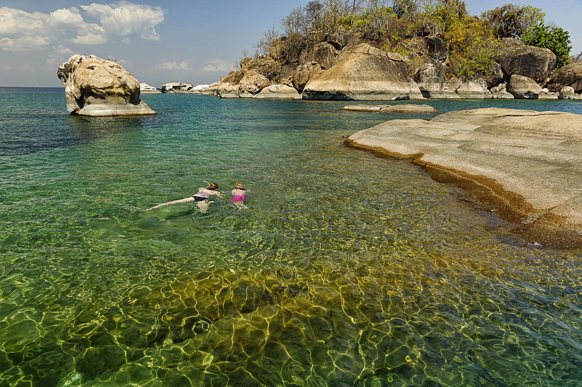 A mother and her daughter snorkeling in crystal clear waters near a rocky islet