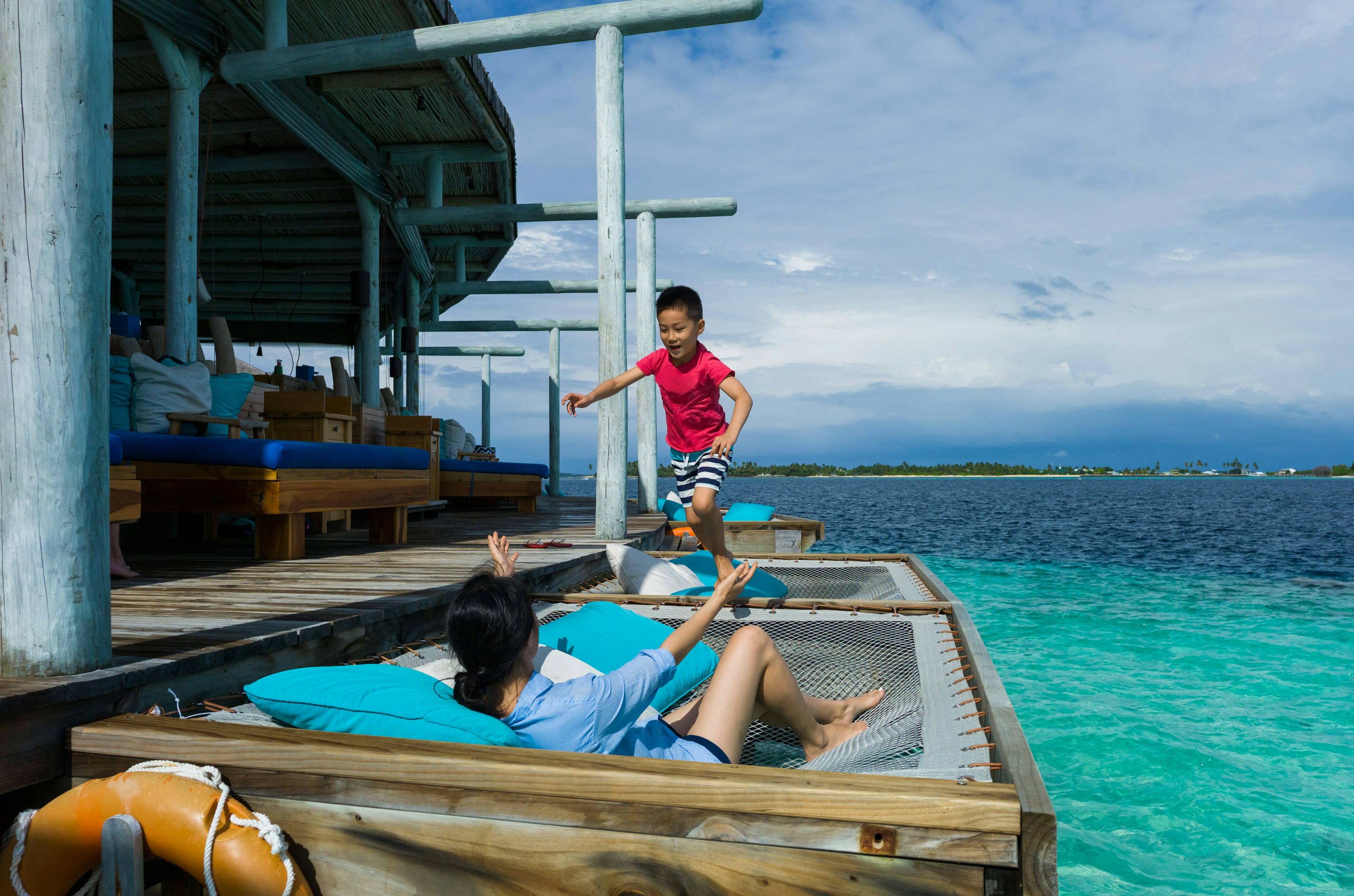 A child jumps across an overwater hammock to his mother at a bungalow in the Maldives