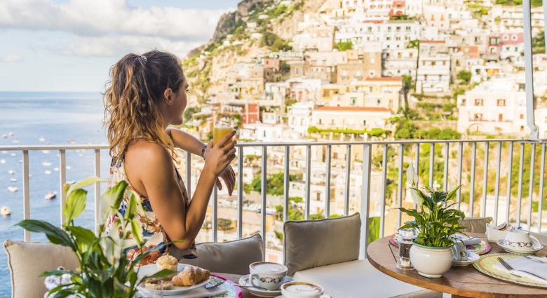 A young woman having breakfast on a balcony in Positano, Italy