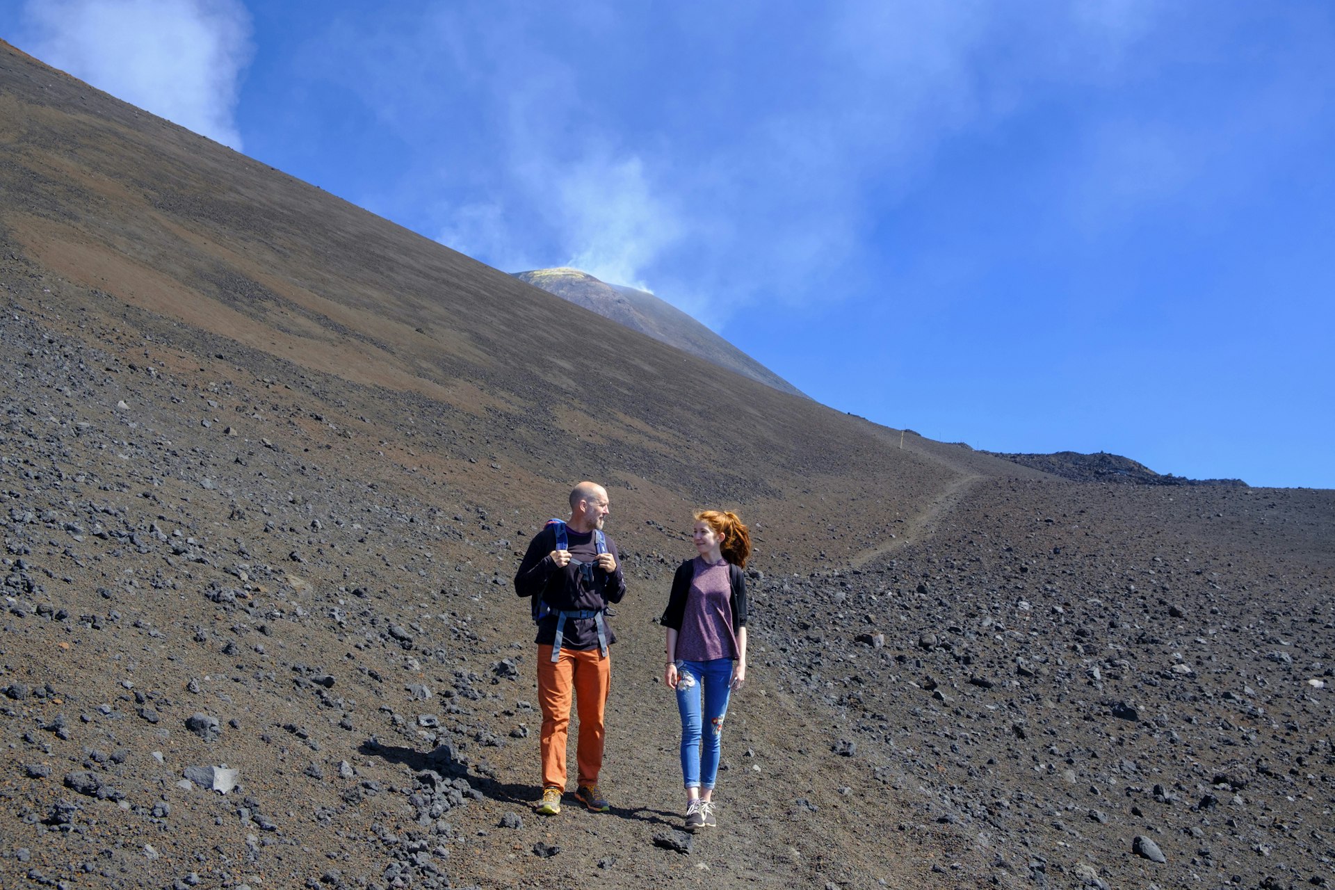 A father and daughter chat as they walk down a volcanic path