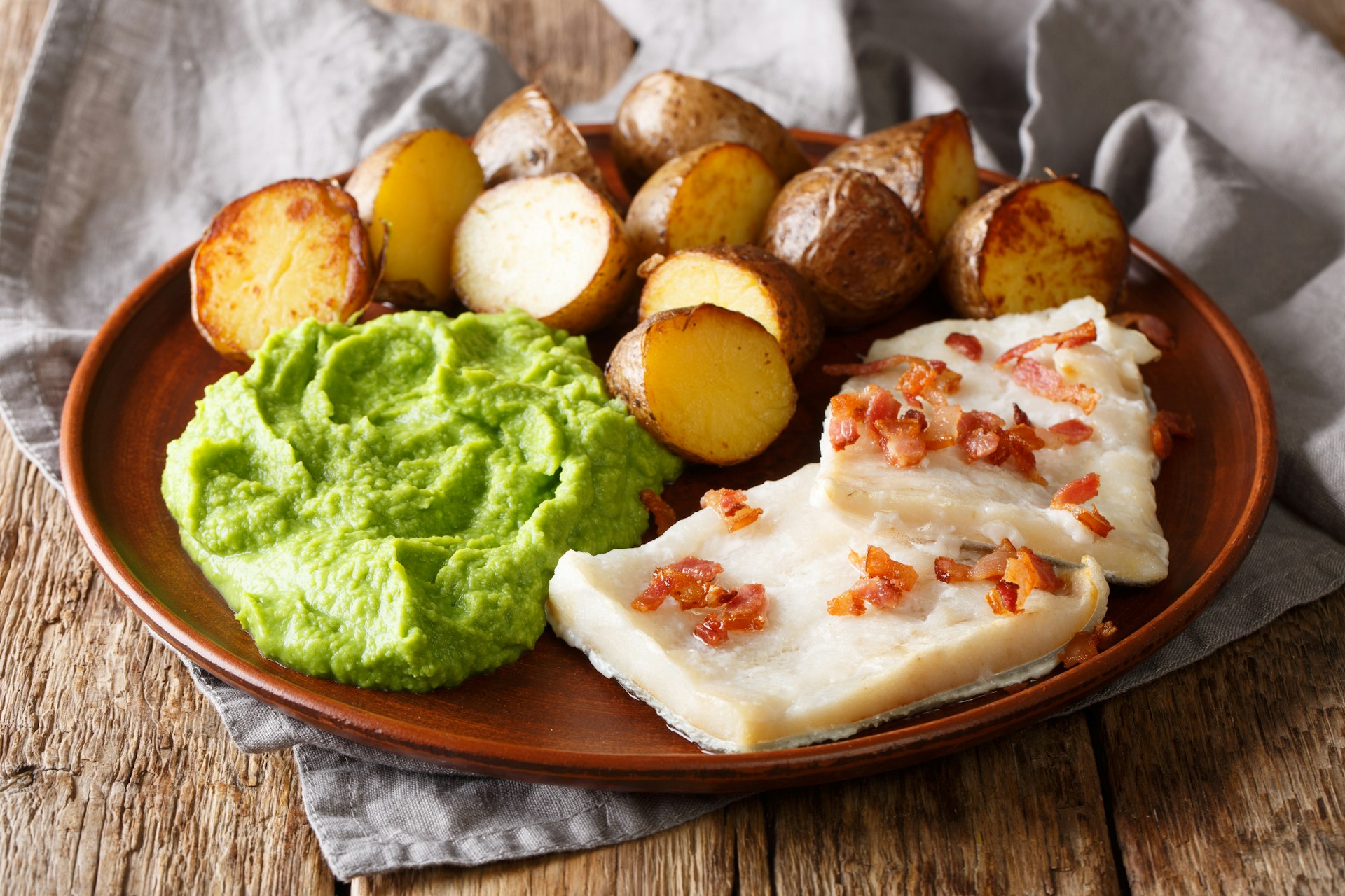 Traditional Scandinavian dish lutefisk, served with pea puree, potatoes and bacon on a plate.