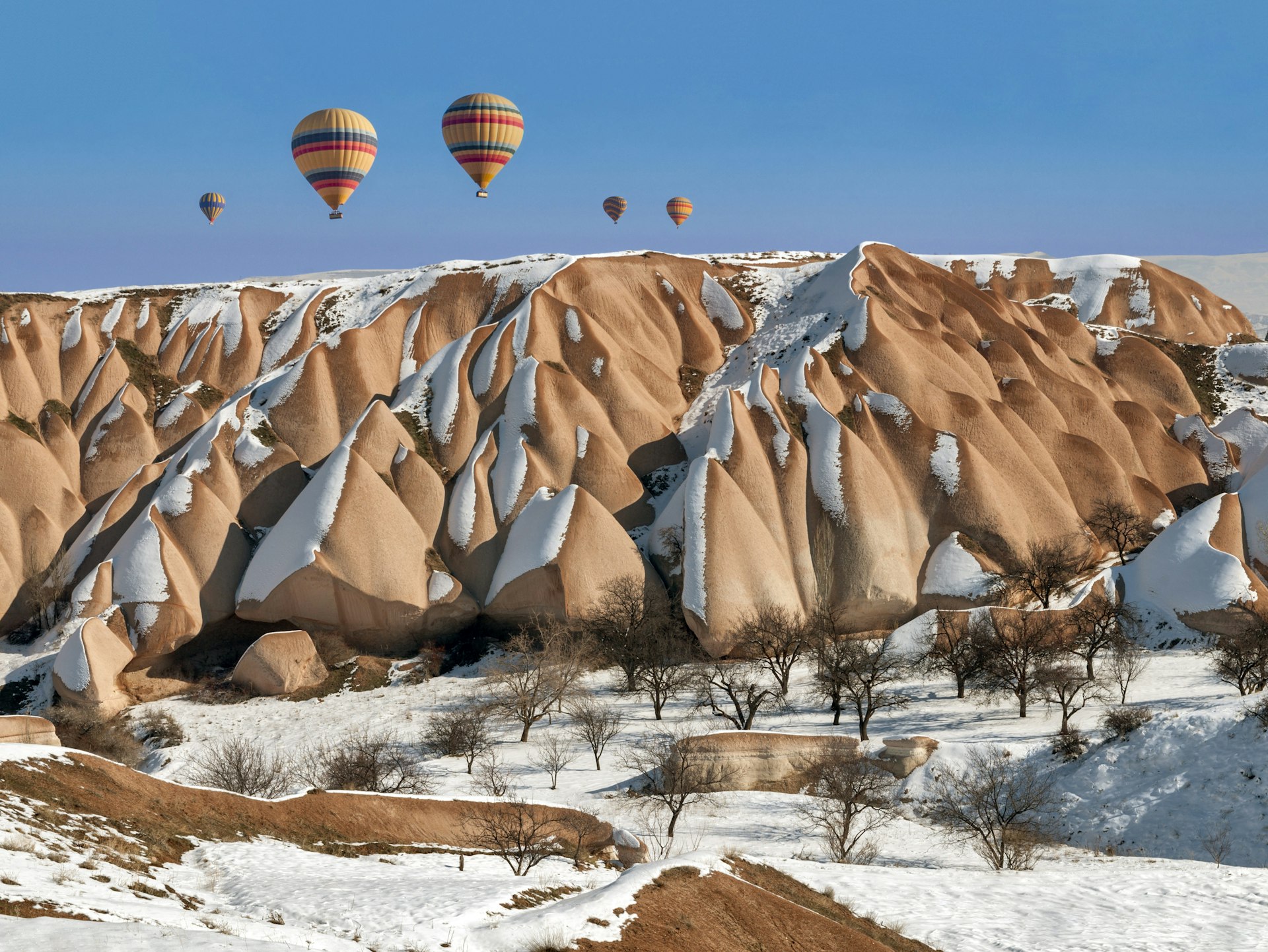 Hot air balloons rising above snow-covered rock formations in Nevsehir.