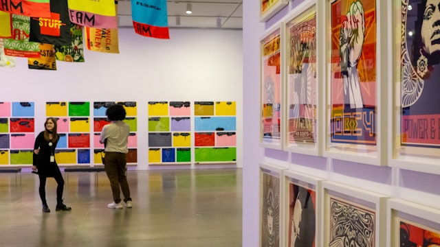 Two people stand in an art gallery lined with prints in bright colors