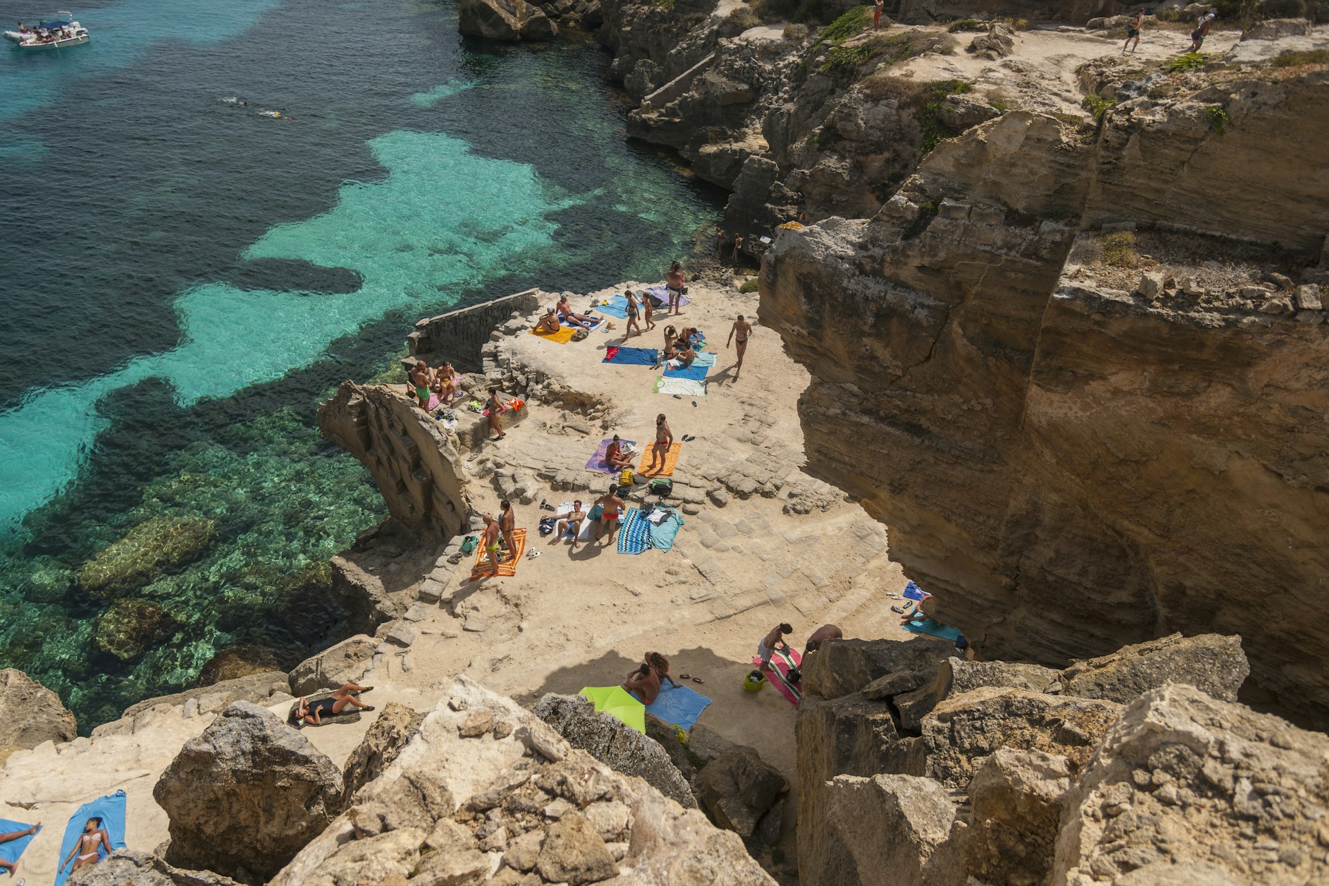 Aerial view of people sunbathing on a cove beach on Favignana, one of the Egadi Islands near Sicily, Italy