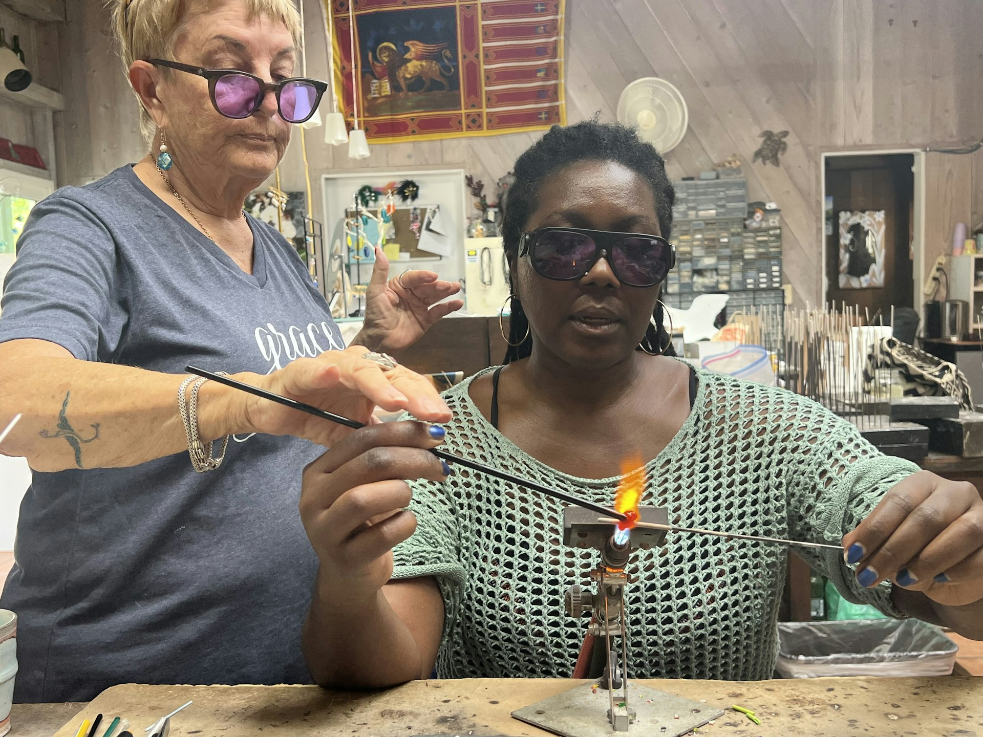 Lonely Planet Destination Editor Alicia Johnson holds two small pieces of metal in front of an open flame as Jobean Chambers of Jobean Glassworks looks on, Saba