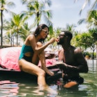 A mixed race couple having cocktails by the pool of a resort in the tropics. She is Asian, he is black. She is feeding him strawberries. Vacation concept.