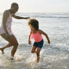 A mom and her daughter play and run in the water at the beach