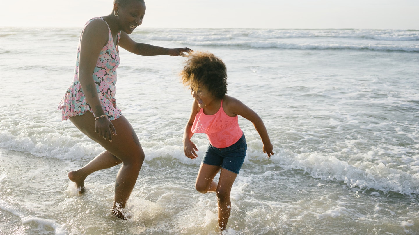 A mom and her daughter play and run in the water at the beach