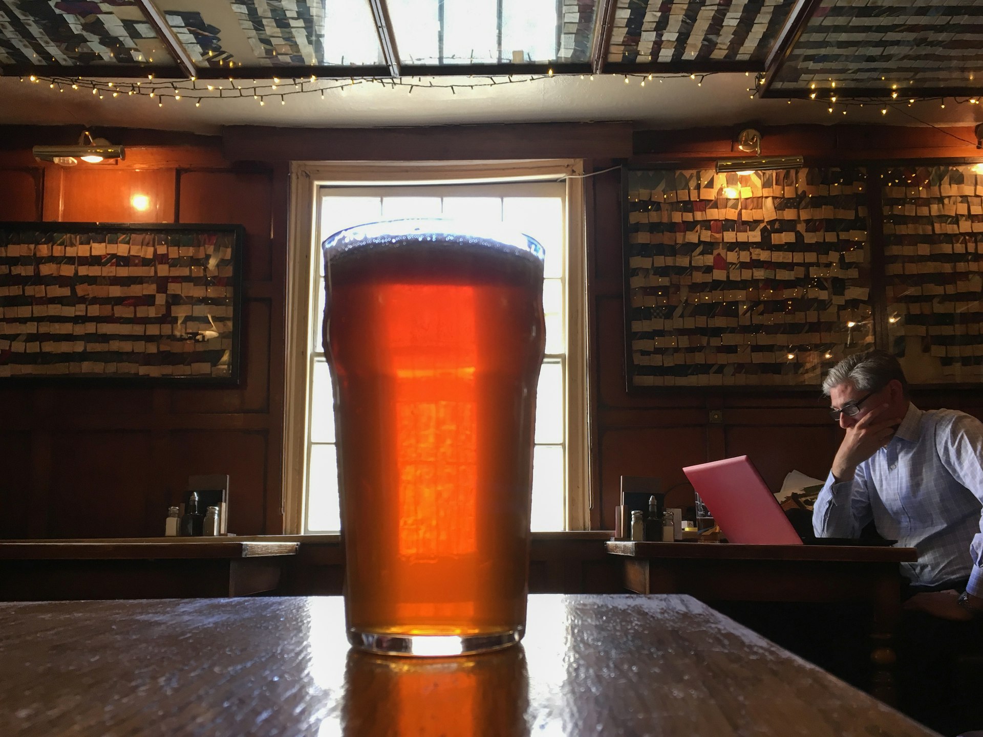 A glass of beer on a table and a man working on his laptop on the background at The Bear Inn pub, Oxford. Founded in 1242, The Bear Inn is the oldest pub in Oxford.