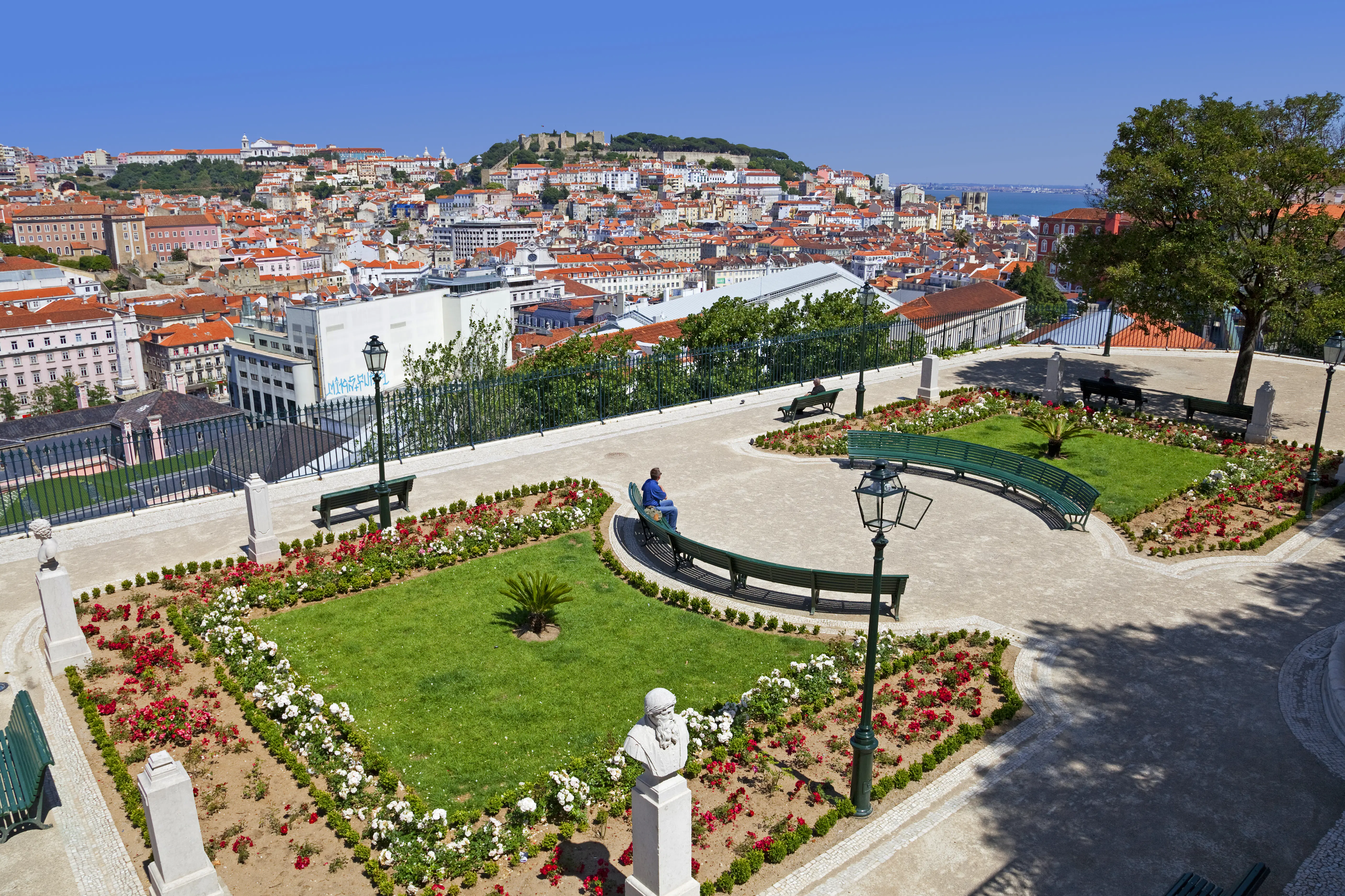 A viewpoint over buildings towards a river, with lawns and flowerbeds