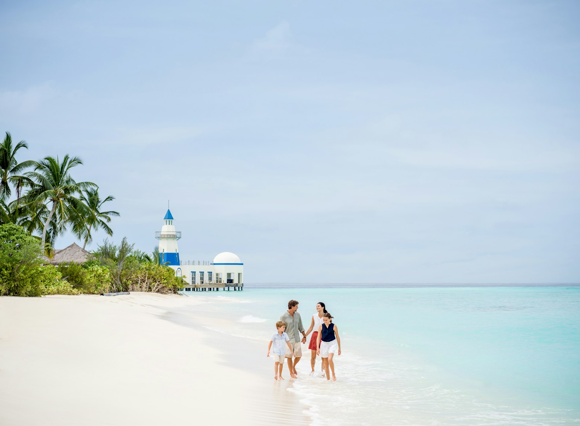 A family on the beach walk in front of the lighthouse at InterContinental Maldives Maamunagau Resort, the Maldives