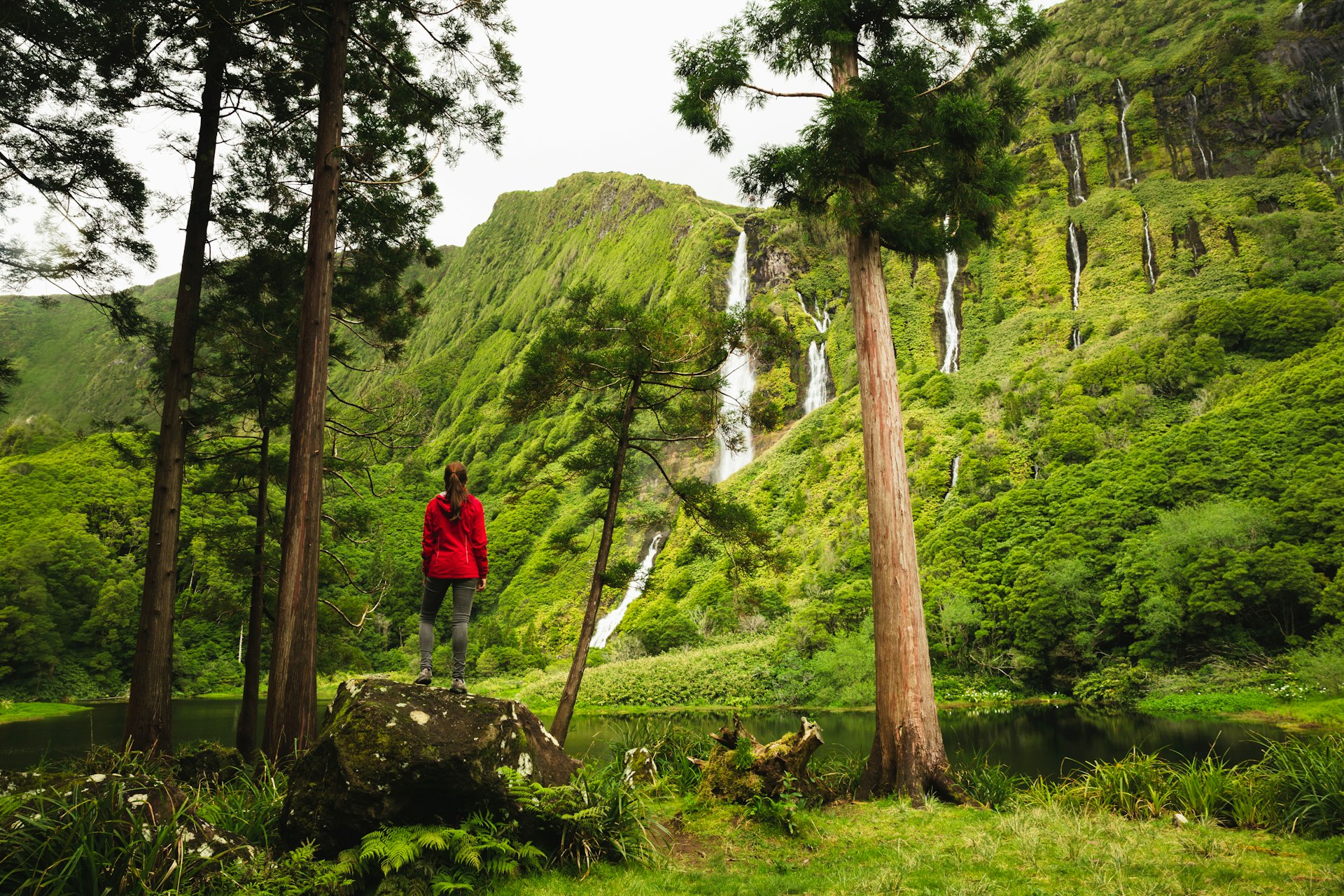A woman looks at waterfalls on a hike in Flores, Azores, Portugal
