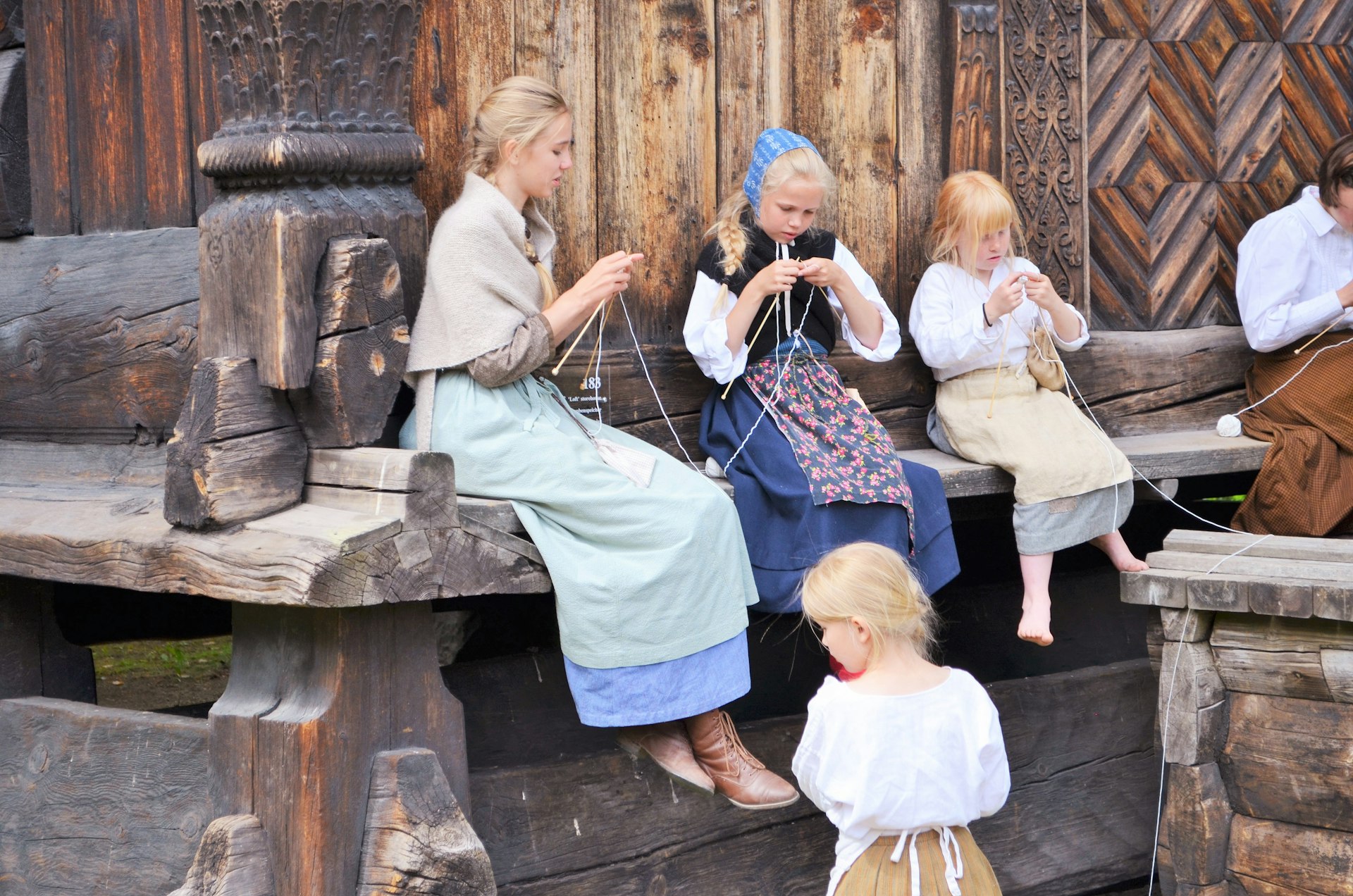 Girls in traditional dress knitting on a wooden porch at the Folkemuseum, Oslo, Norway
