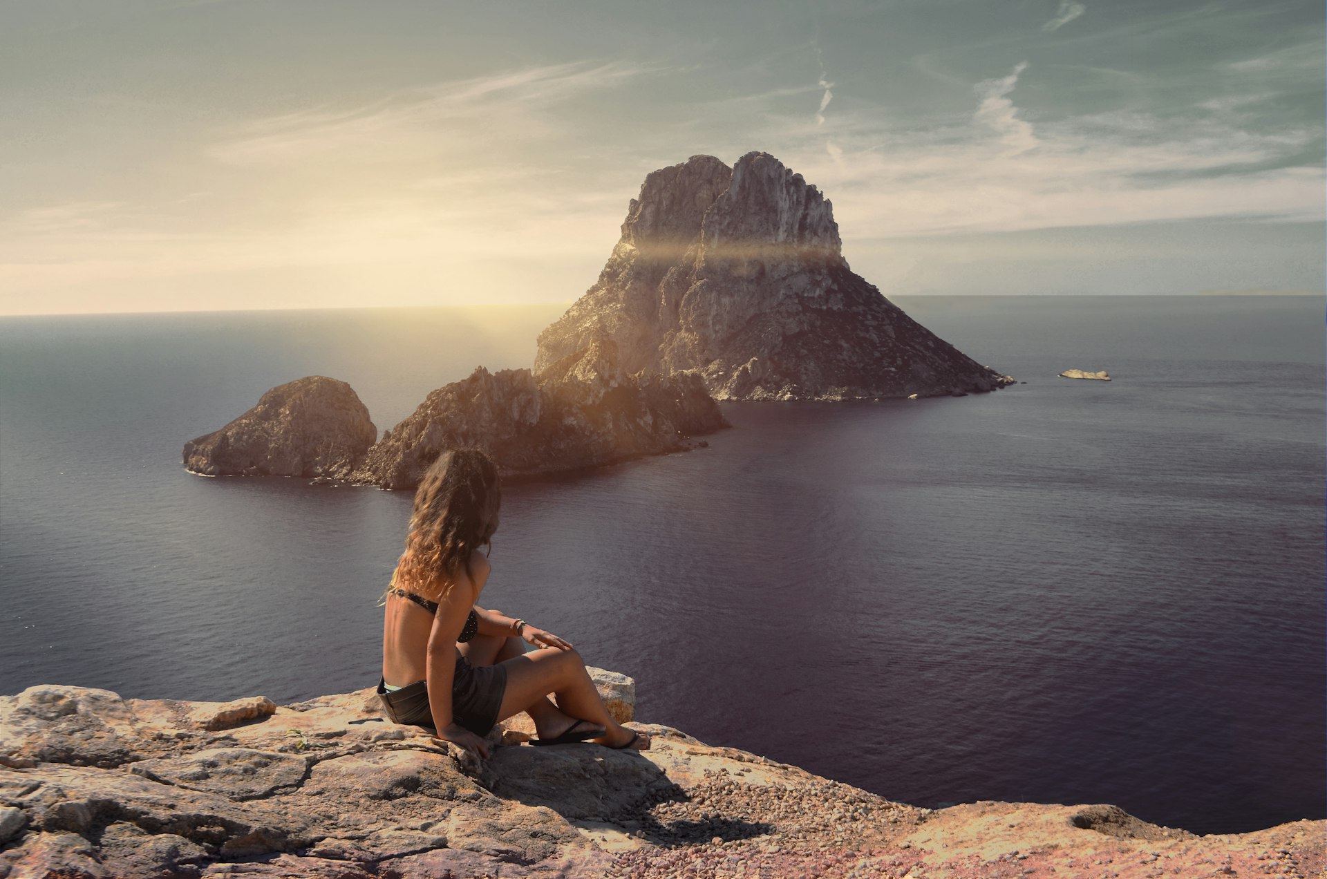 A woman looks at the rocky island of Es Vedrà at sunset, Ibiza, Balearic Islands, Spain