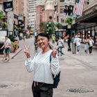 An Asian woman smiling and making the peace sign at the Downtown Crossing in Boston, USA.