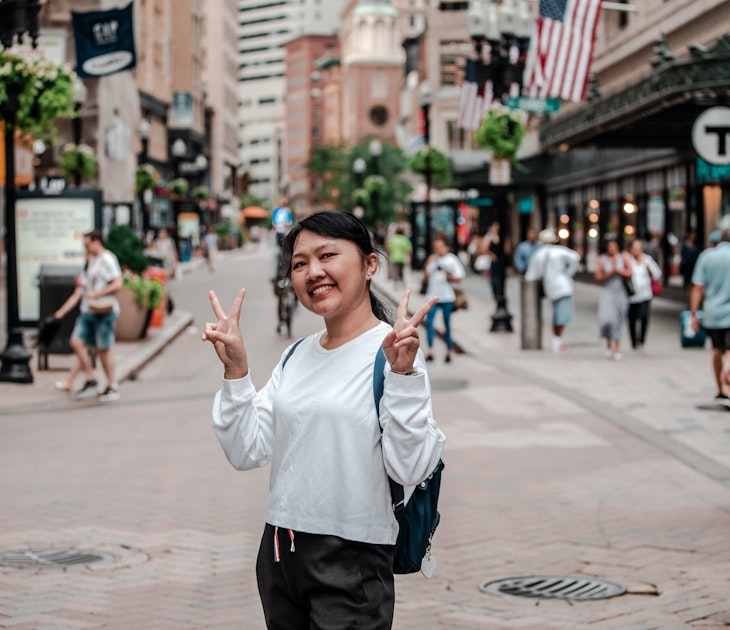 An Asian woman smiling and making the peace sign at the Downtown Crossing in Boston, USA.
