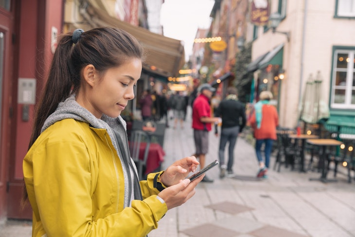 Woman using mobile phone app while walking down the street in Québec City, Canada