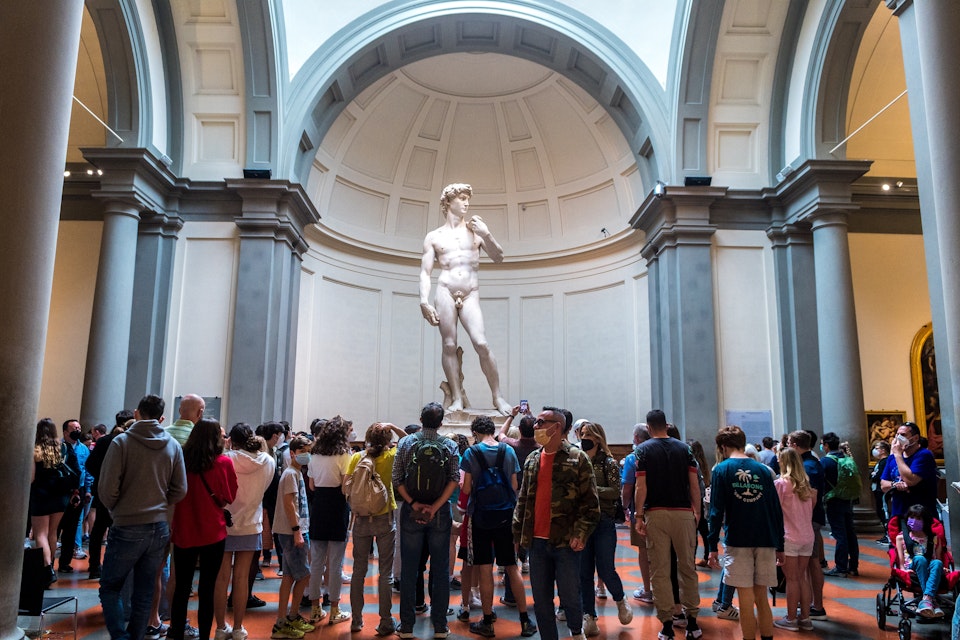 Crowded gallery by tourists trying to take photo to david sculpture in accademia.