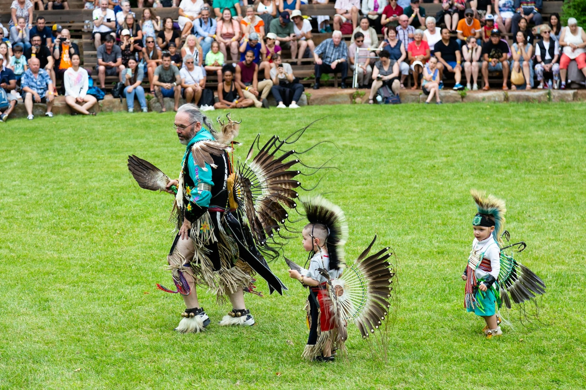 A man and two small Indigenous boys dressed in ceremonial costume for the annual pow wow dancing in Wendake, Québec