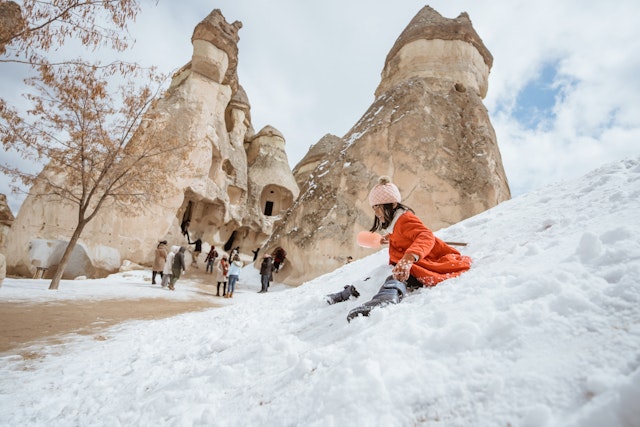 A little girl slides down the snow on the fairy chimneys in Cappadocia.