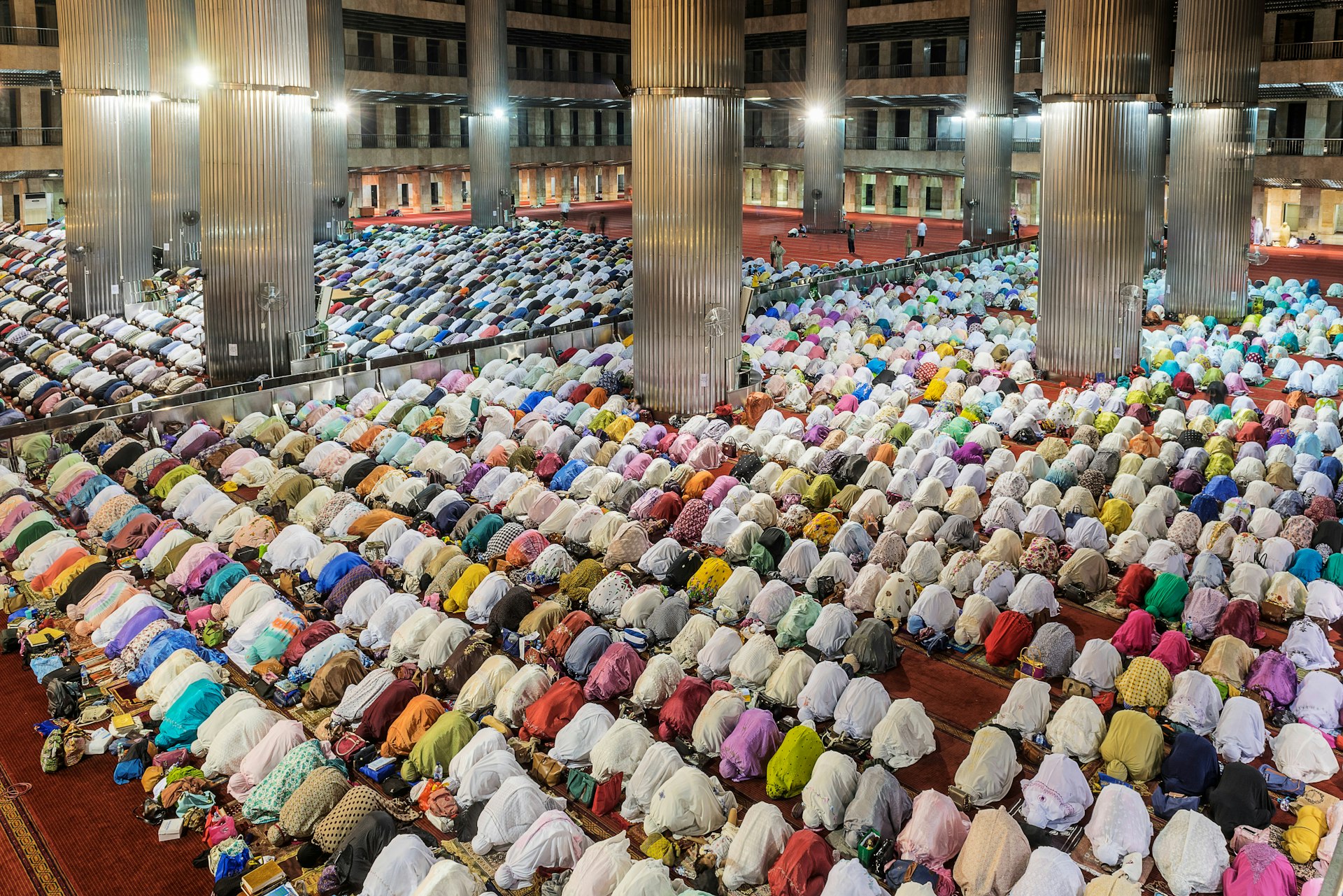 People kneeling forward in prayer during Ramadan; men on one side of the mosque, women on the other