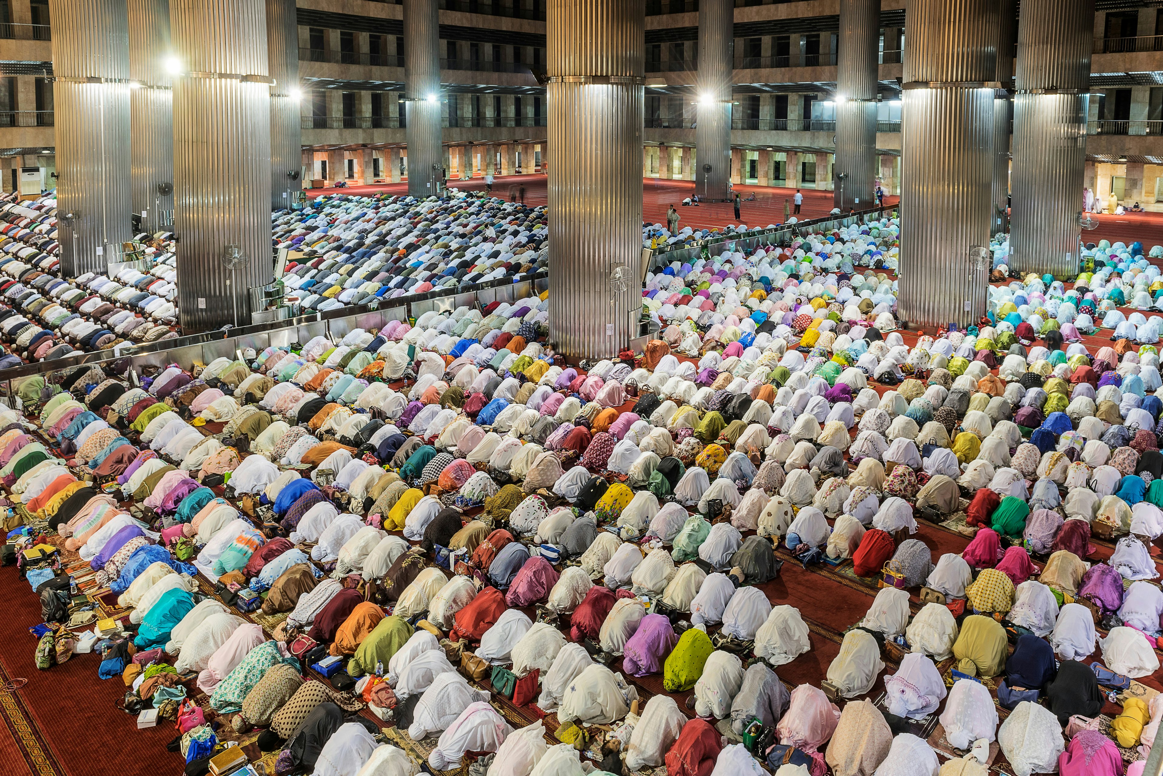 People kneeling forward in prayer during Ramadan; men on one side of the mosque, women on the other