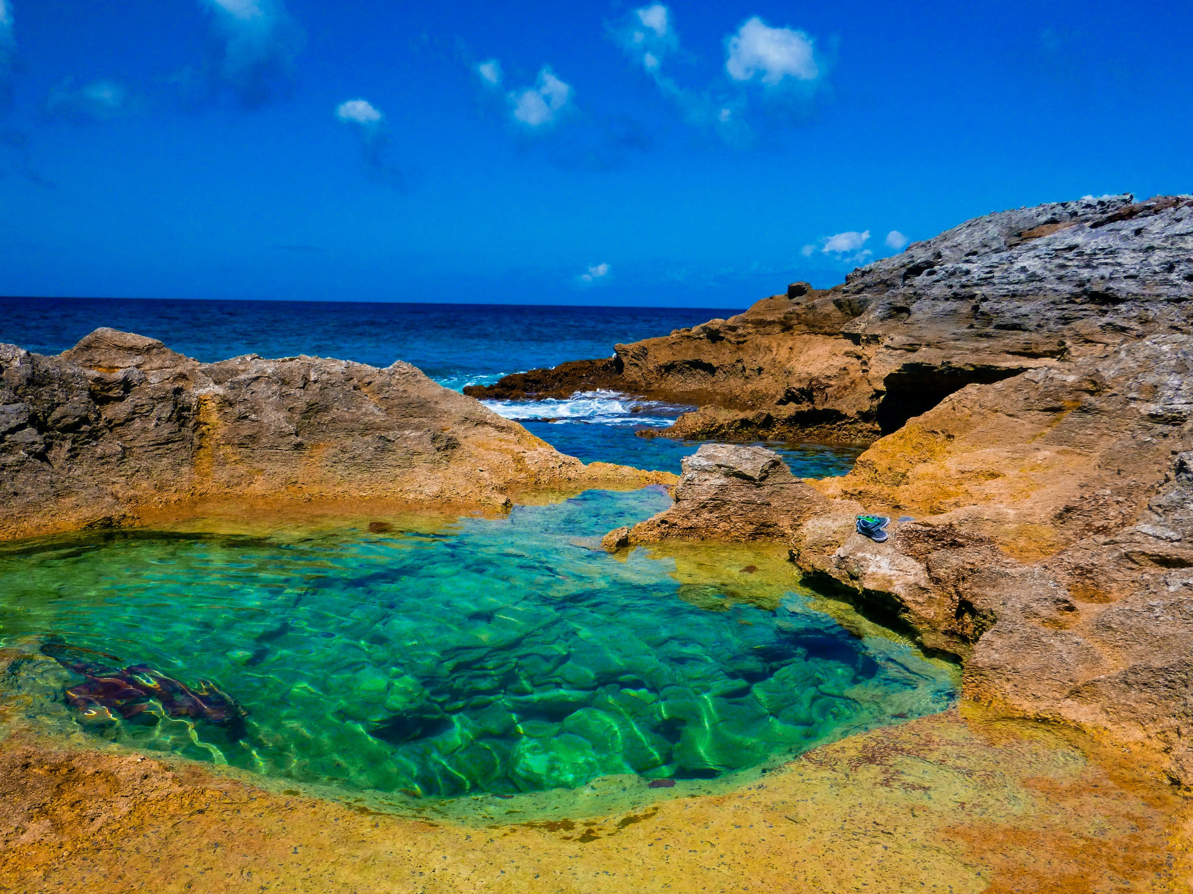 A blue ocean pool surrounded by rocks with a small gap leading to the ocean