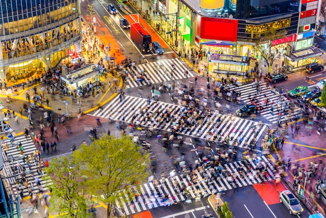 An aerial view of the Shibuya Crossing, one of the busiest crosswalks in the world, with the lit up buildings around it