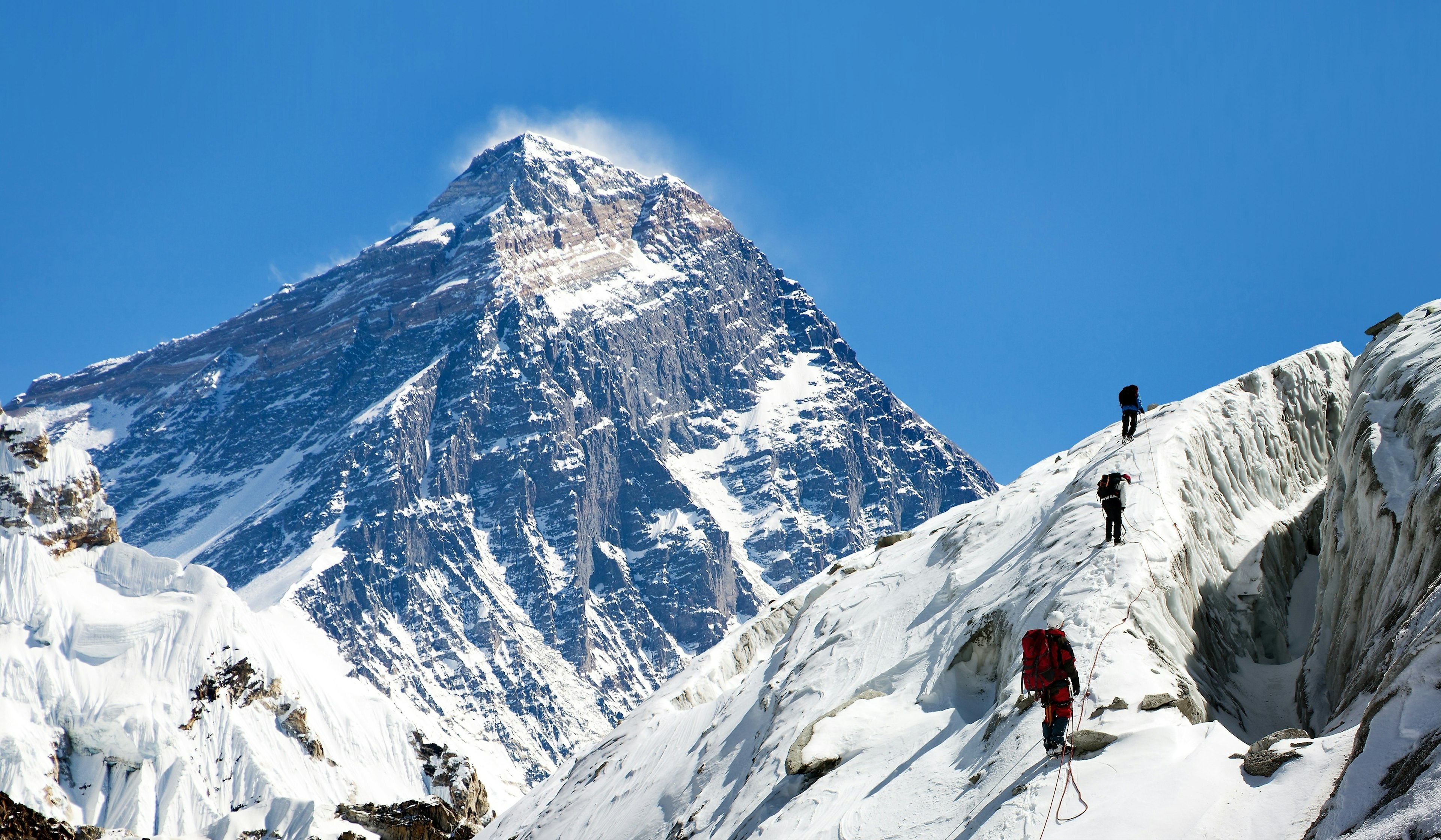 Mountaineerers climb a glacier trail with ropes to support them