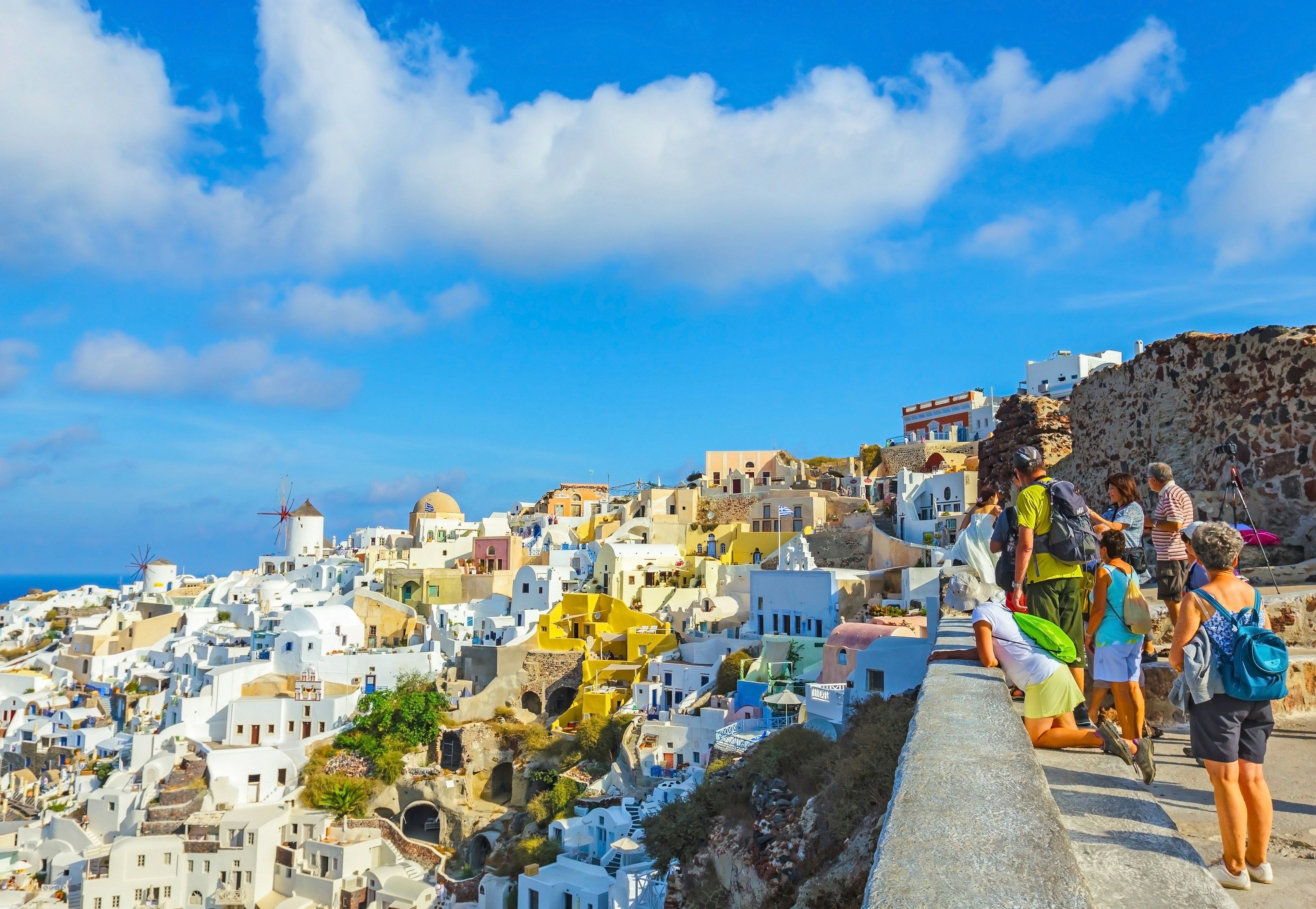 A small group of tourists gather to look at the view over the white buildings built into the cliffs in Santorini