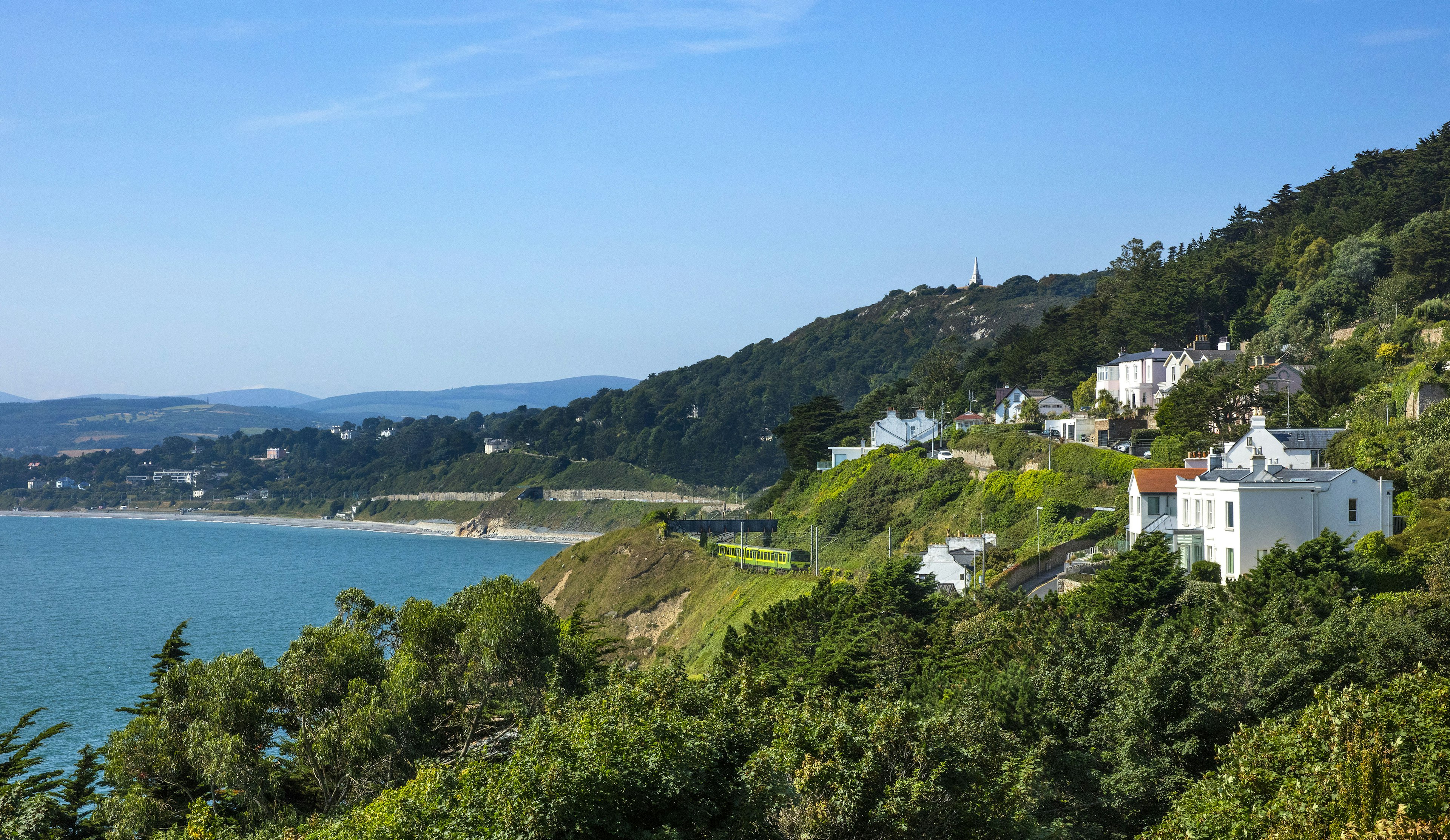 A train runs through a village near the edge of the sea